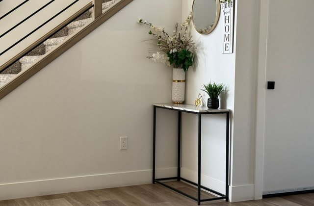 A narrow entryway with a console table and mirror beneath a staircase
