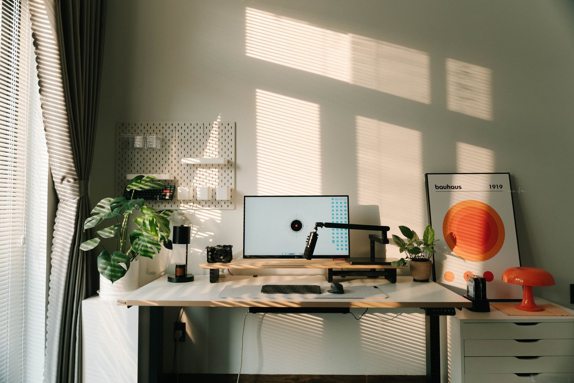 A home office desk beside a window, with plants and a sage green wall