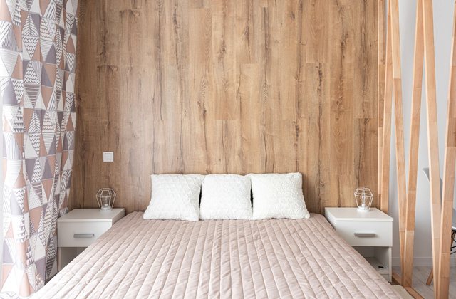 A calm bedroom with pale bedding and a wooden wall behind the bed