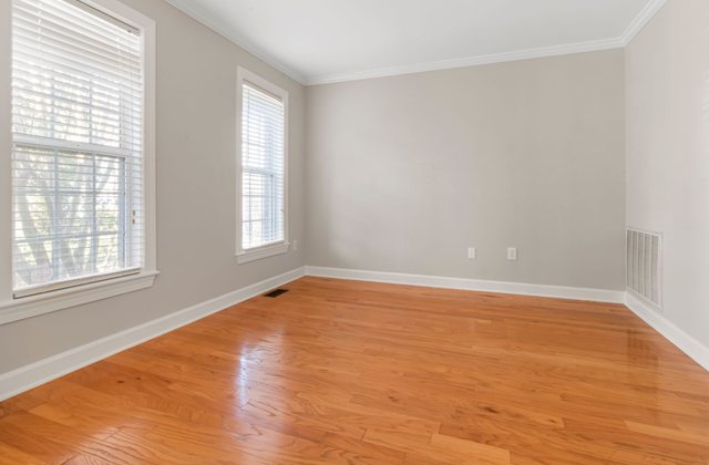 An empty room with a hardwood floor and daylight from two windows