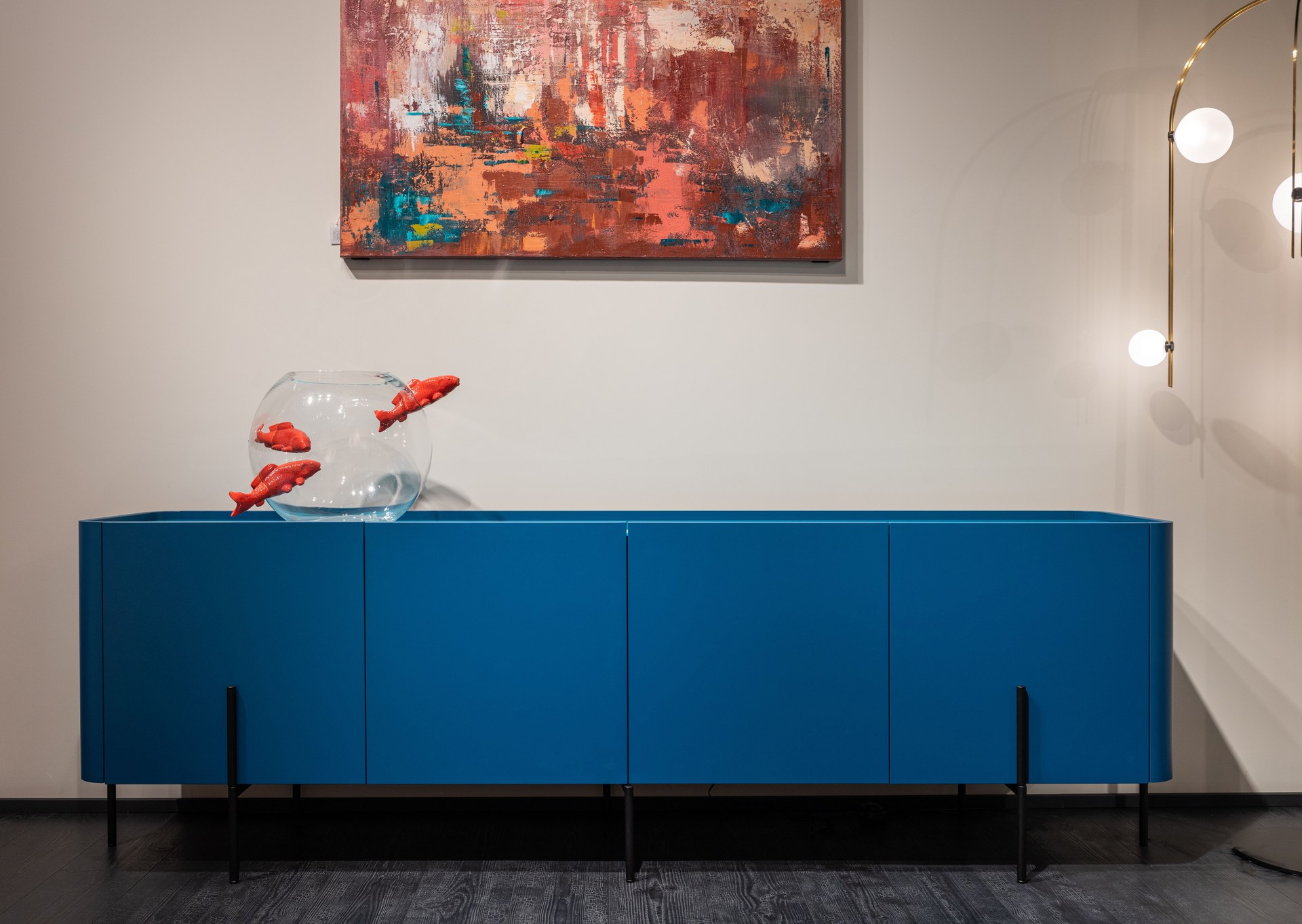 Modern blue cupboard with glass aquarium decorated with fish placed at white wall with creative picture in modern room with glowing lamps