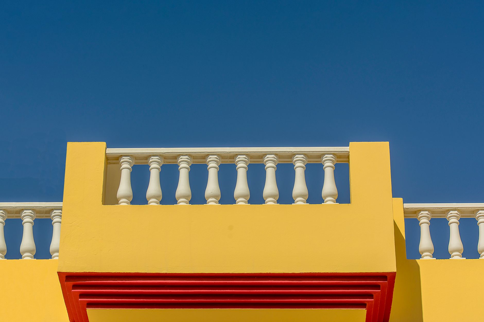 Vibrant yellow balcony with white balustrades against a clear blue sky, illustrating What Does Feng Shui Say About a Balcony or Terrace
