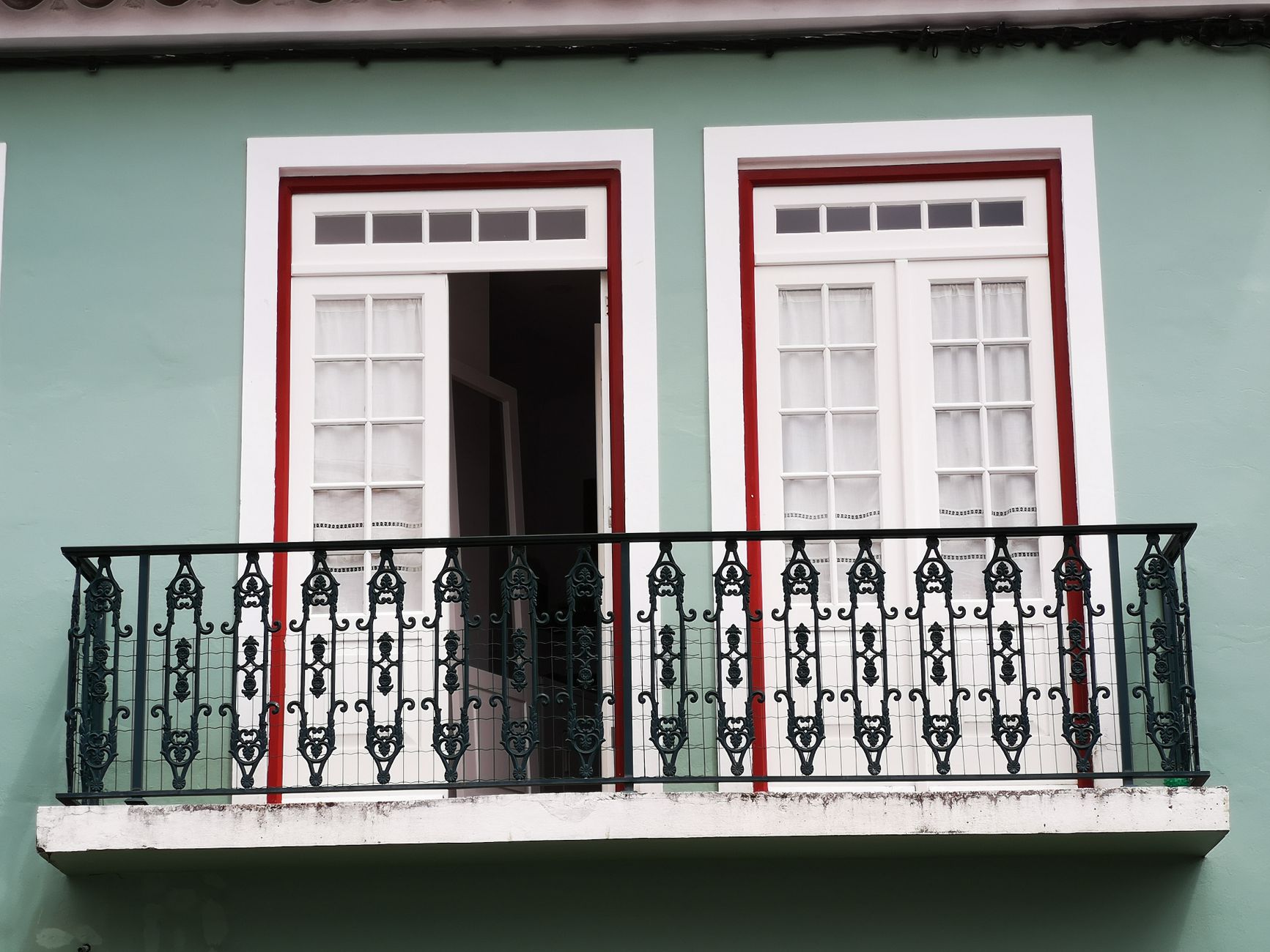 A beautifully designed balcony with ornate ironwork and white French doors on a green facade, illustrating What Does Feng Shui Say About a Balcony or Terrace