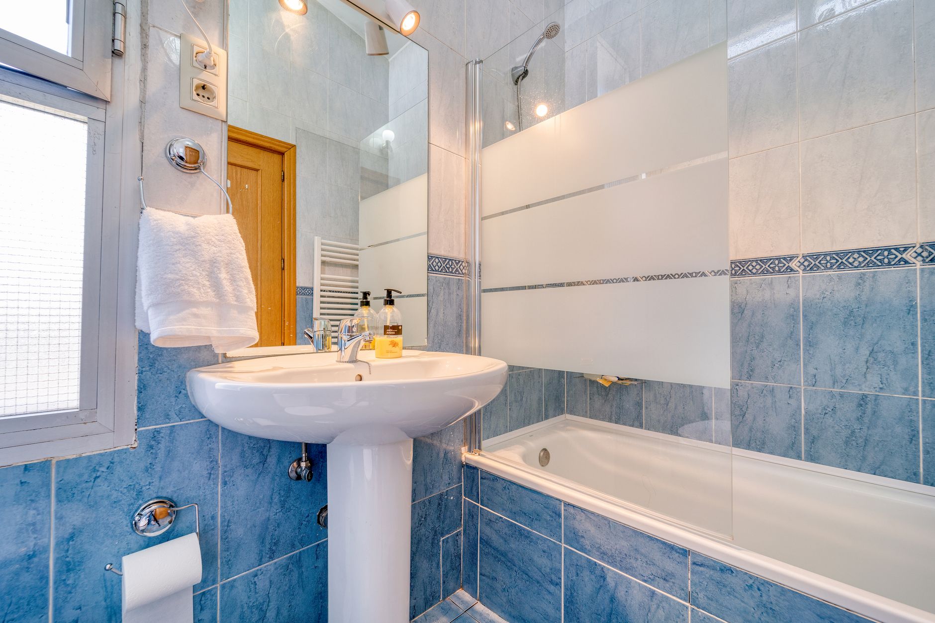 Bright minimalist bathroom with modern blue tiles, glass shower, and a clean white sink, illustrating What Does Feng Shui Say About a Bathroom Door
