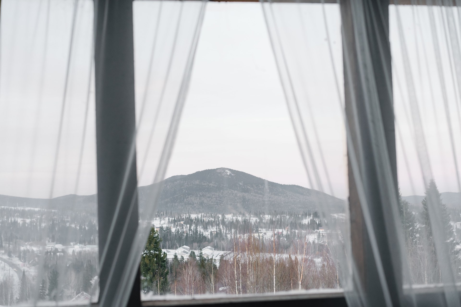 Winter landscape framed by sheer curtains, showcasing snow-covered mountains and forests