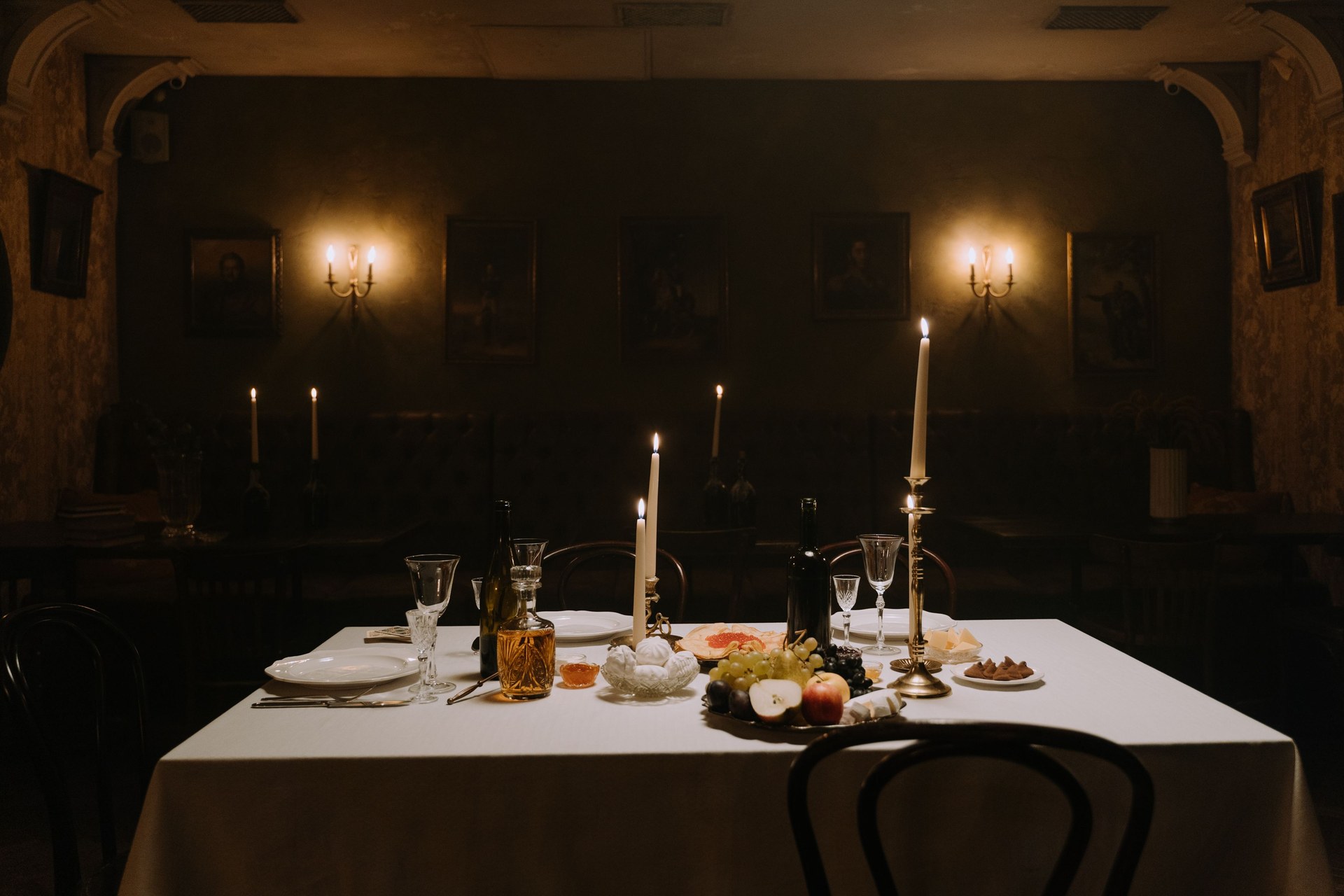 A dimly lit dining room with elegantly set table, decorated with candles, wine, and fruits for a cozy atmosphere