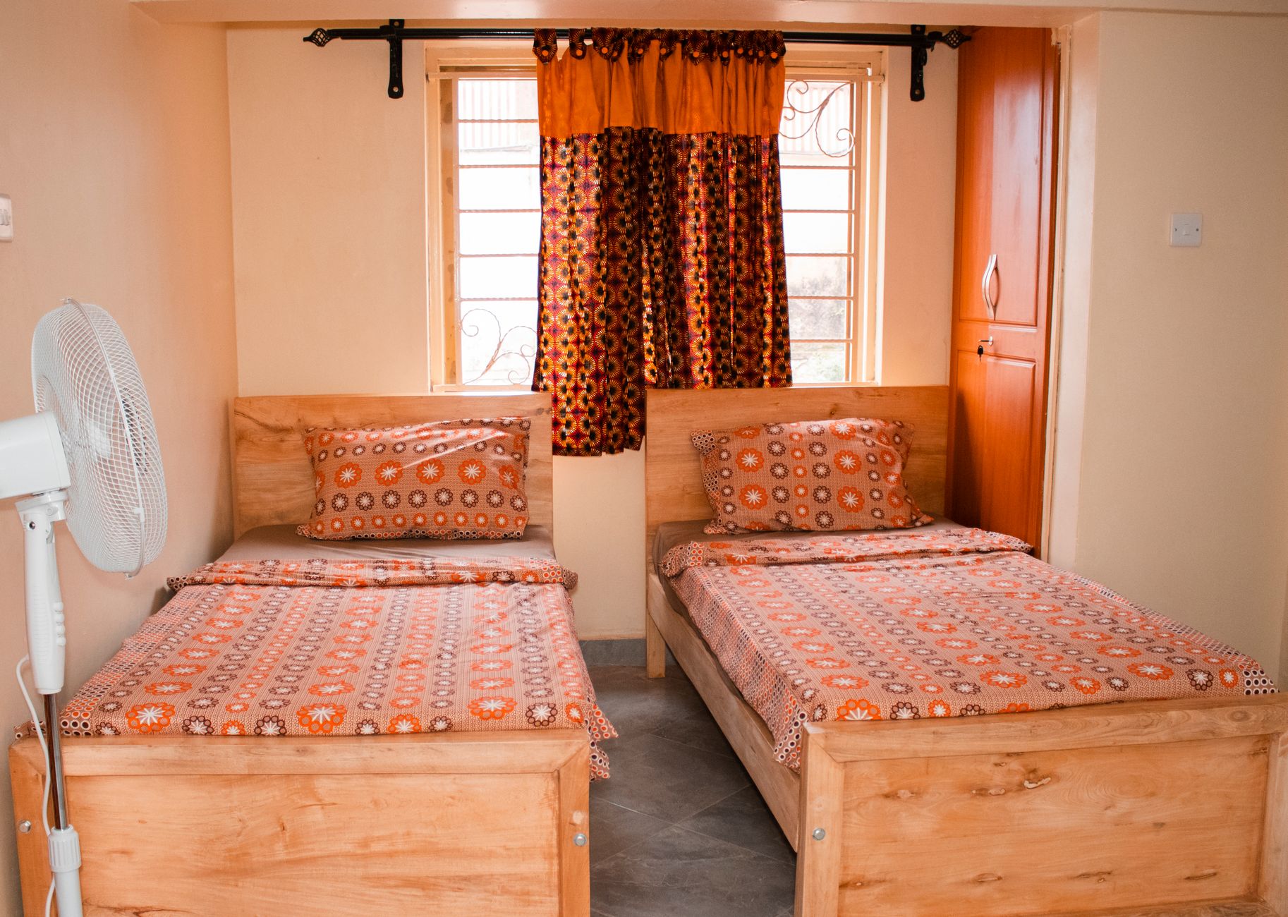 A brightly lit twin bedroom in Kampala, Uganda, featuring matching patterned bedding and wooden furniture, illustrating Can't Move the Bed? What Feng Shui Actually Suggests