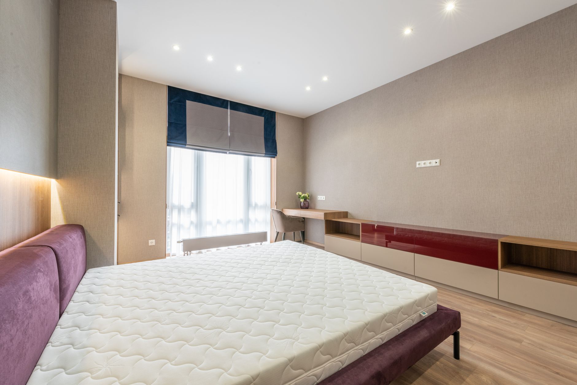 Modern bedroom with white mattress on bed placed against wooden cabinet and table with flowerpot at wall with roller blind on window, illustrating What Does Feng Shui Say About Mir