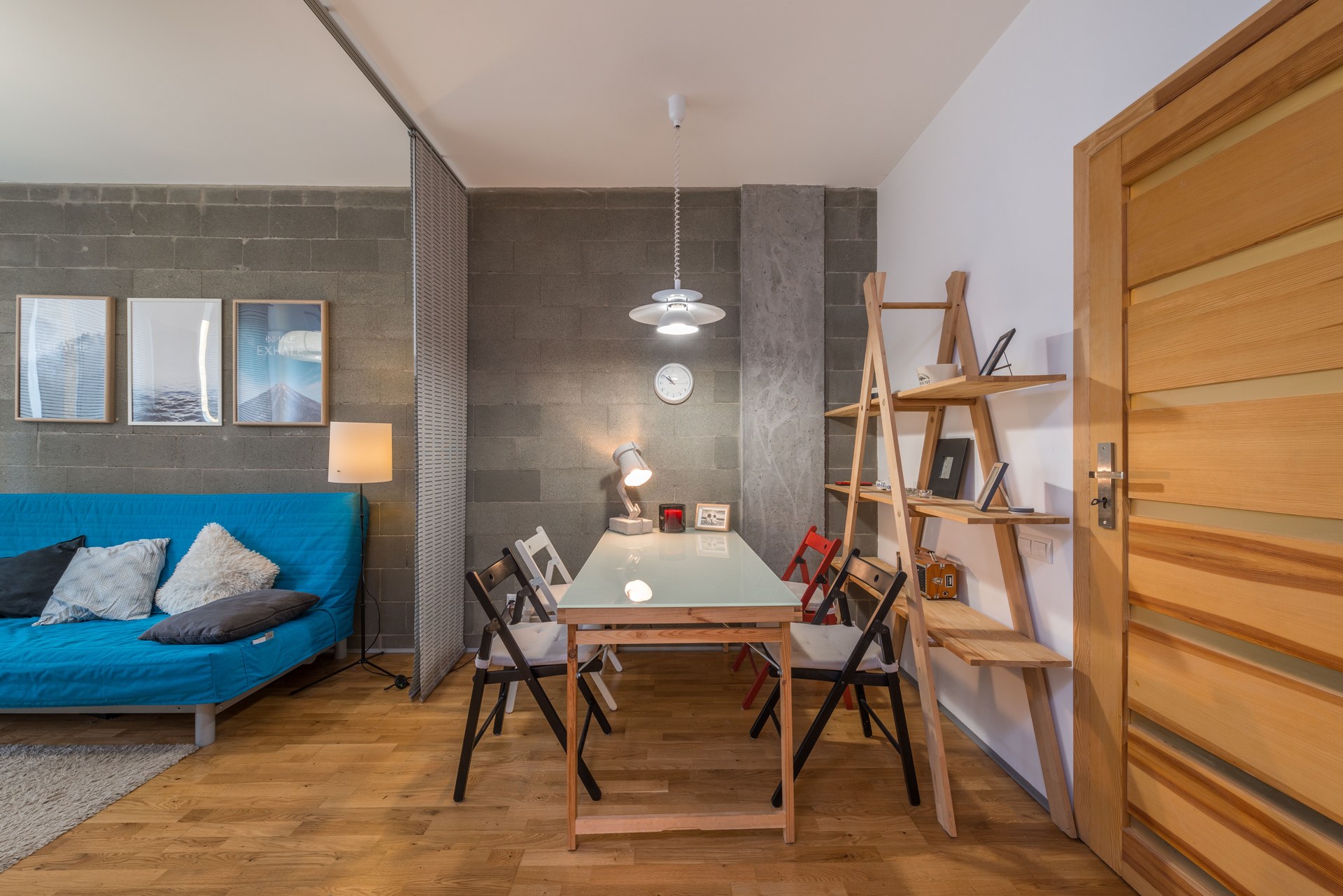 Big wooden table with colorful chairs near shelves in cozy modern living room with sofa