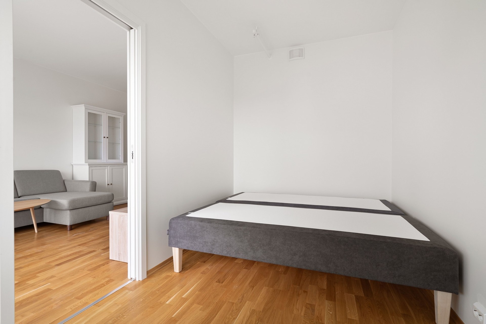 Spacious minimalist bedroom featuring a modern sofa and bed frame with wooden parquet flooring