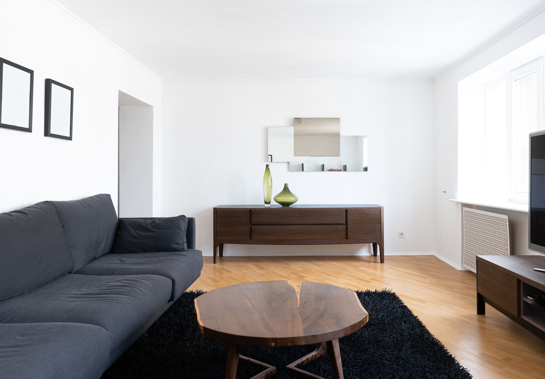Interior of modern light home with couch near wooden table on carpet near cabinets with vases and TV, illustrating How to Apply Feng Shui in a Studio Apartment