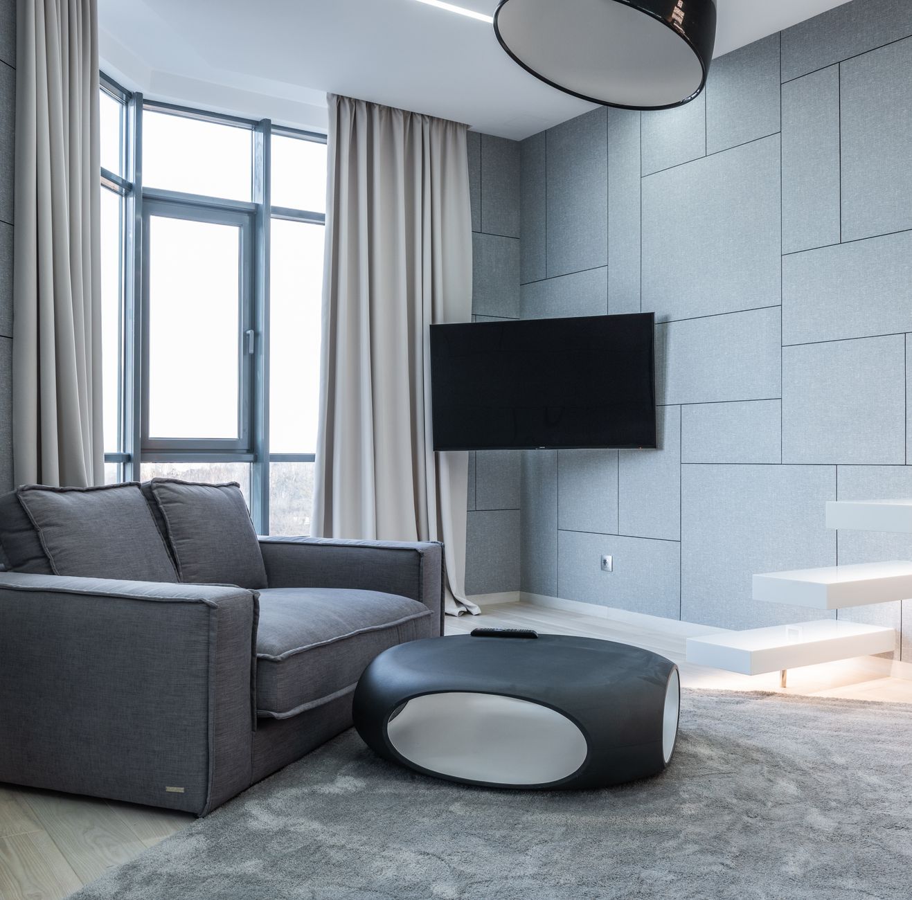 Interior of living room with gray sofa near table on carpet and windows with curtains near TV and white stairs — illustrating Form School vs Compass School Feng Shui: The Differenc