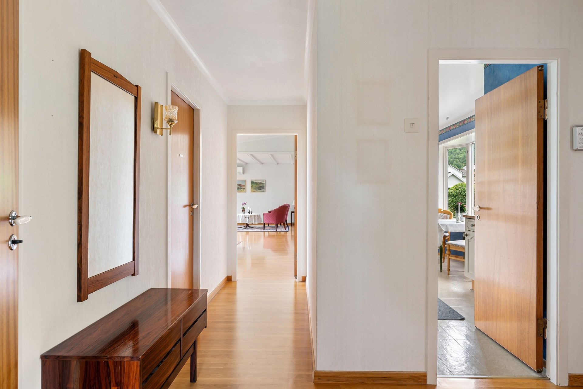 A well-lit modern hallway with open doors leading to a bright living area and garden view