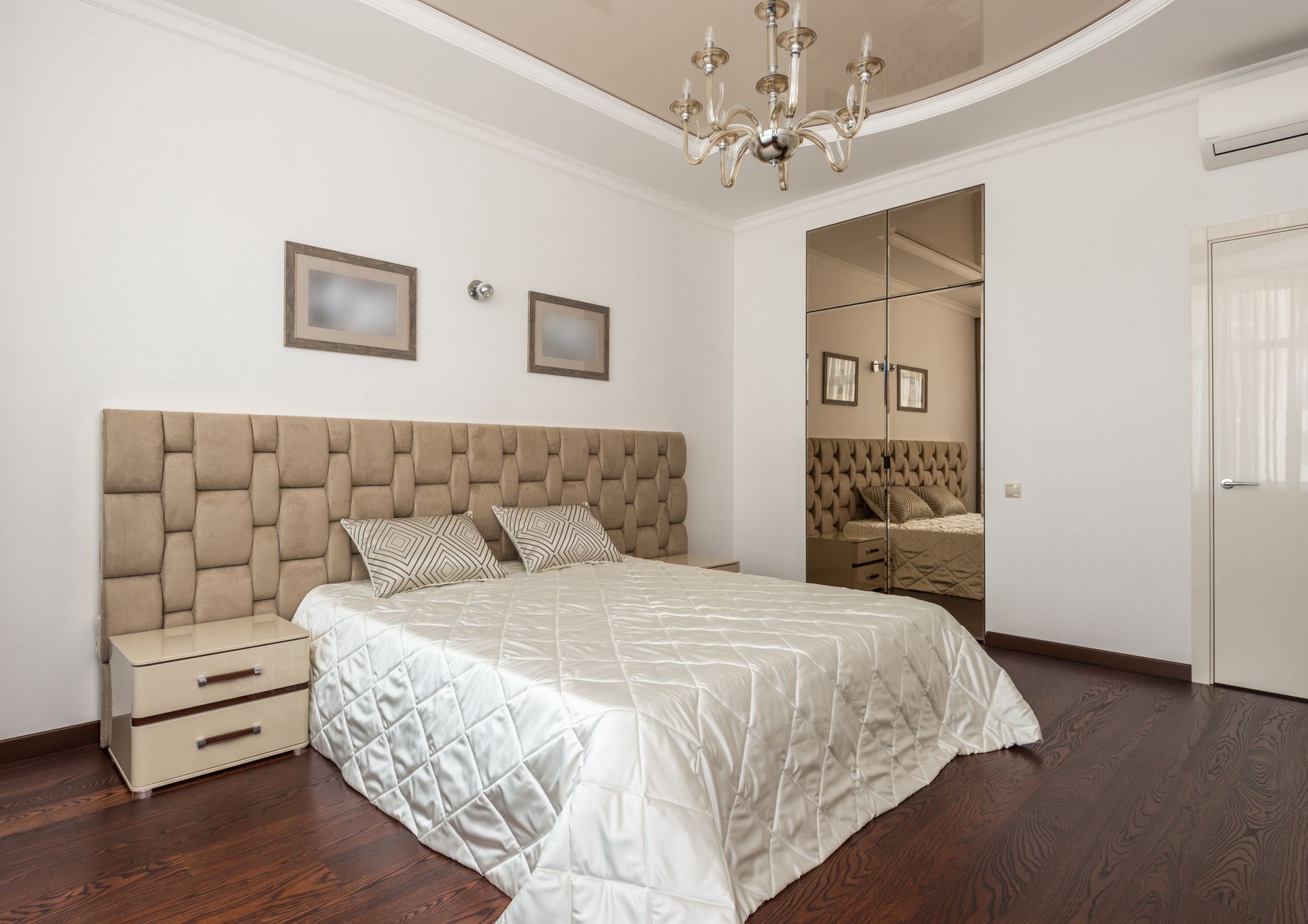 Stylish modern bedroom with plush headboard, chandelier, and mirrored closet doors, illustrating What Does Feng Shui Say About a Guest Bedroom