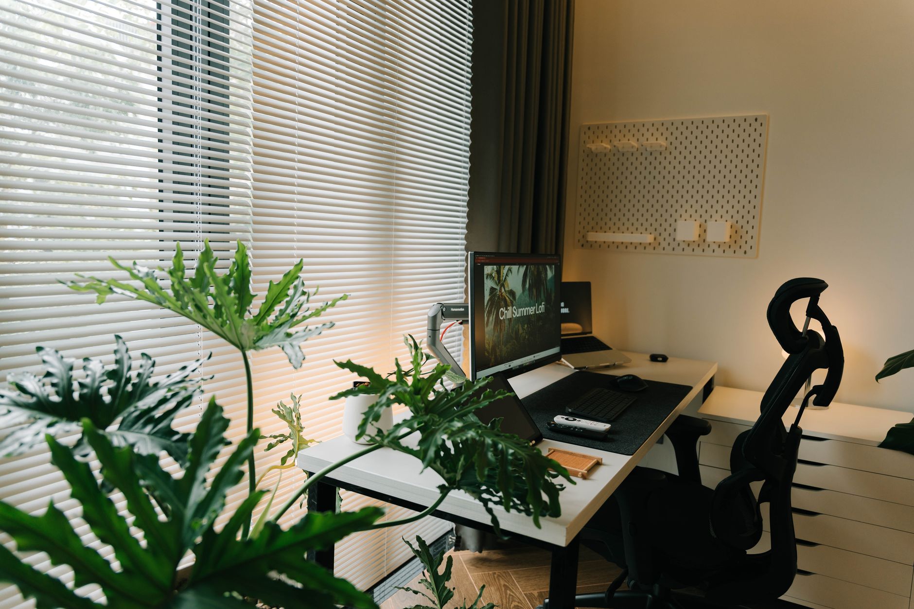 A stylish home office with a desk, chair, and lush green plants near a window with blinds, illustrating Where Should a Home Office Desk Face? Feng Shui Guide