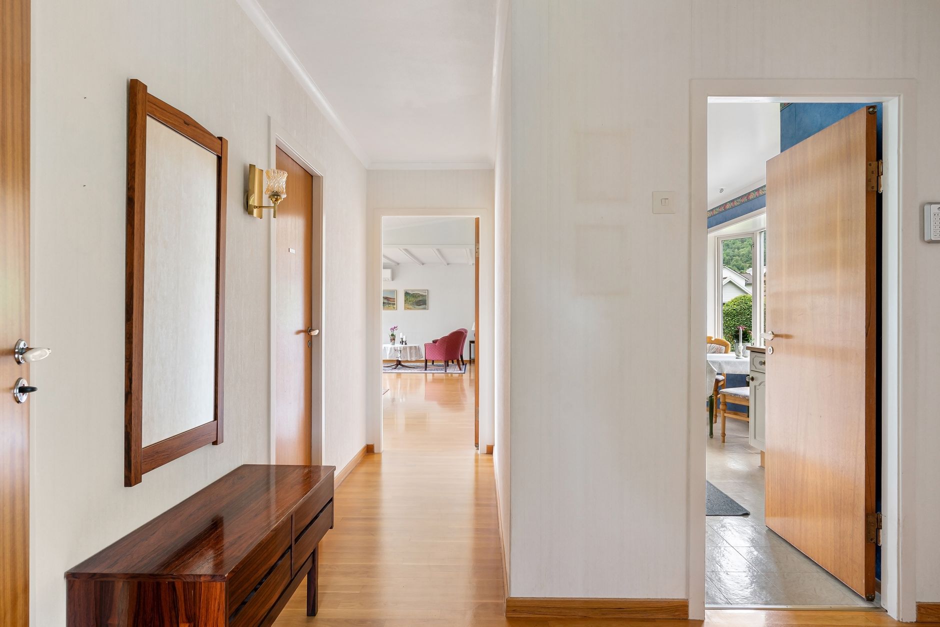 A well lit modern hallway with open doors leading to a bright living area and garden view, illustrating How Do You Handle a Home With No Hallway