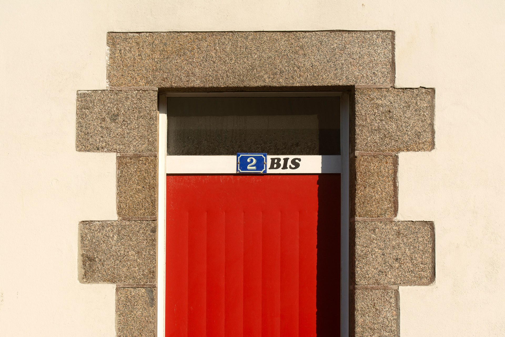 Close-up of a red door with number 2 BIS on a stone-framed building facade