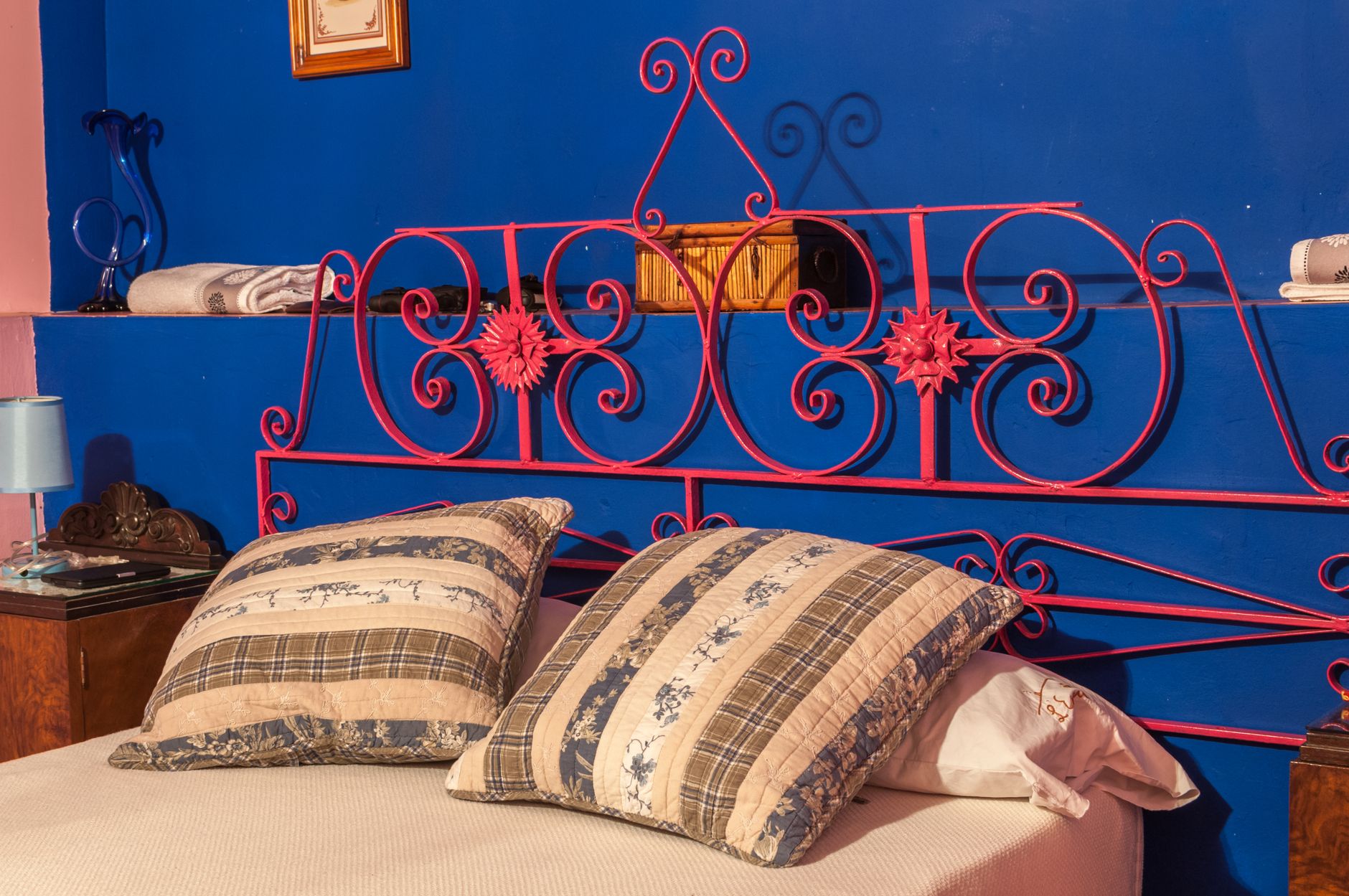 A cozy bedroom featuring a red wrought iron headboard against a blue wall with stylish decor, illustrating How Should a Headboard Be Positioned? A Feng Shui Guide