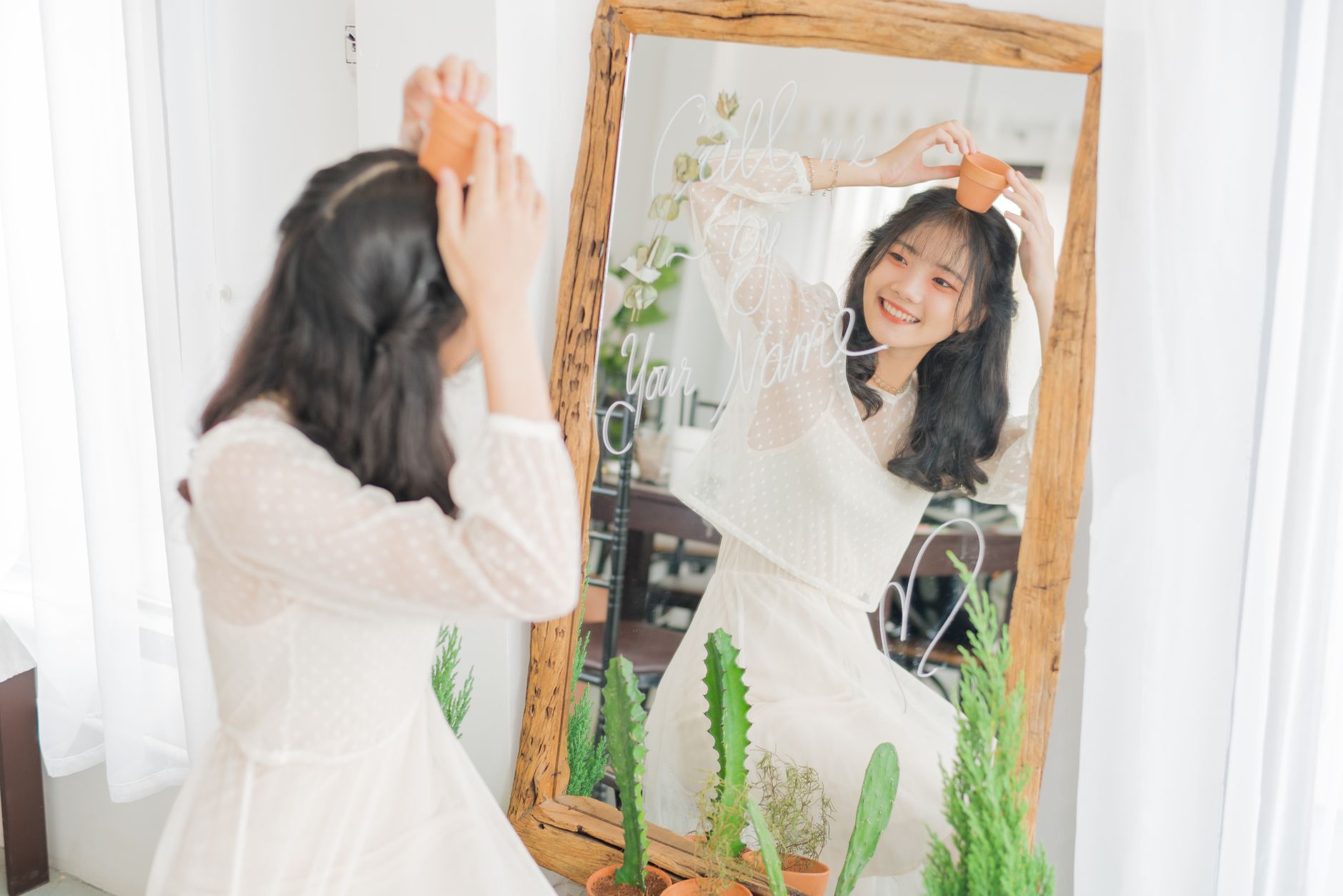 Smiling woman holding a small pot in front of mirror with plants, embracing nature indoors, illustrating Mirror Facing the Bed: Is It Actually a Feng Shui Problem