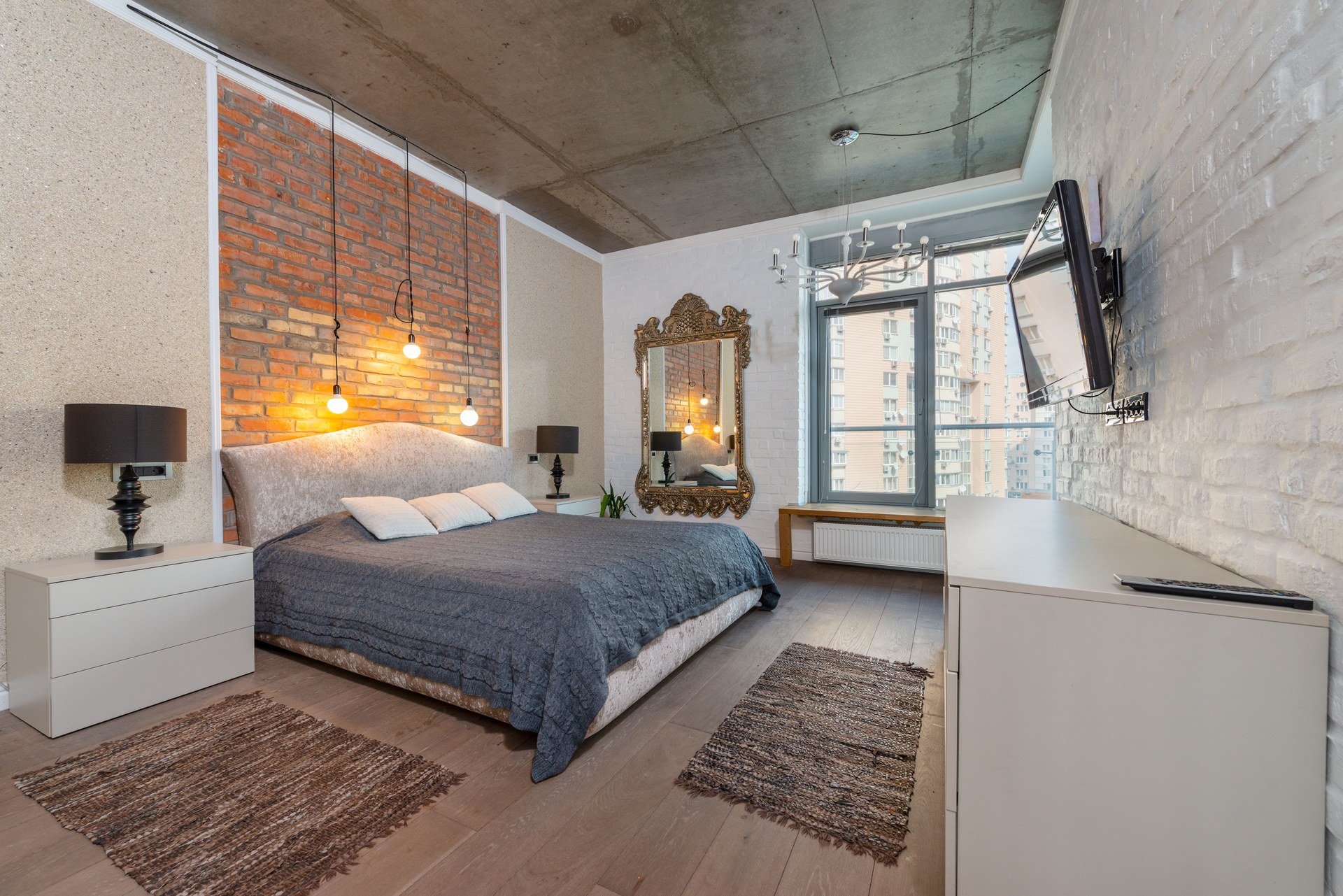 Spacious industrial-style bedroom with brick wall, cozy bed, and modern decor