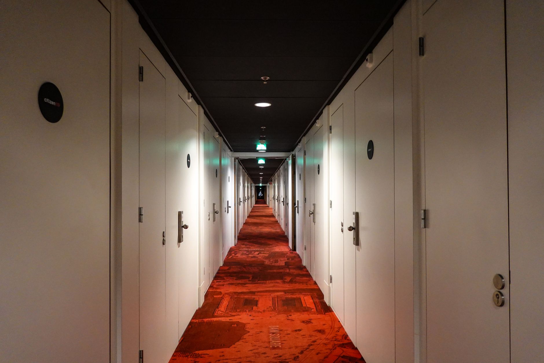 Long, symmetrical hotel hallway with red carpet and closed white doors under warm lighting, illustrating Narrow Hallway Feng Shui: How Should It Be Handled