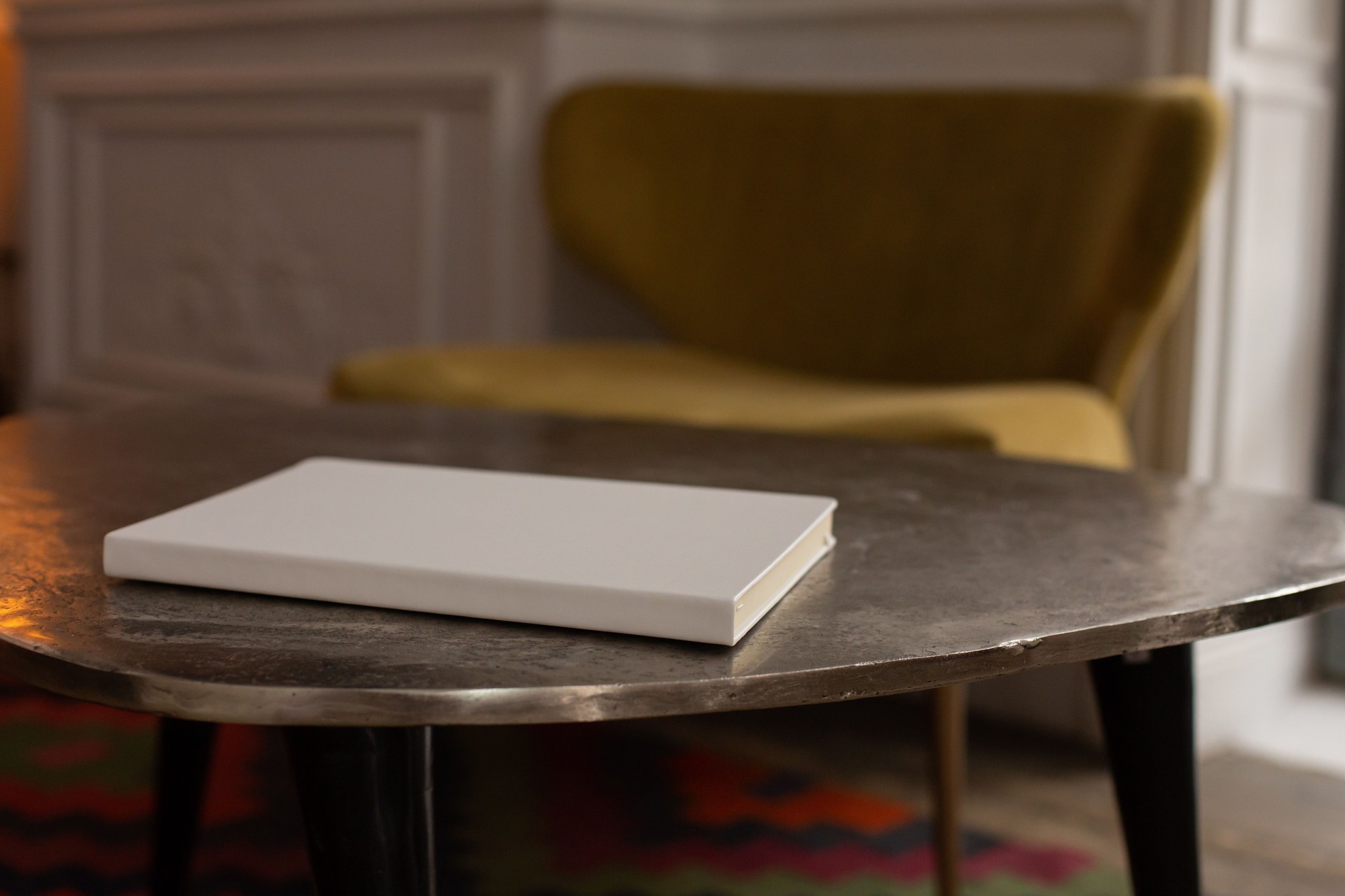 Interior of vintage room with white book placed on black table located near green velvet armchair