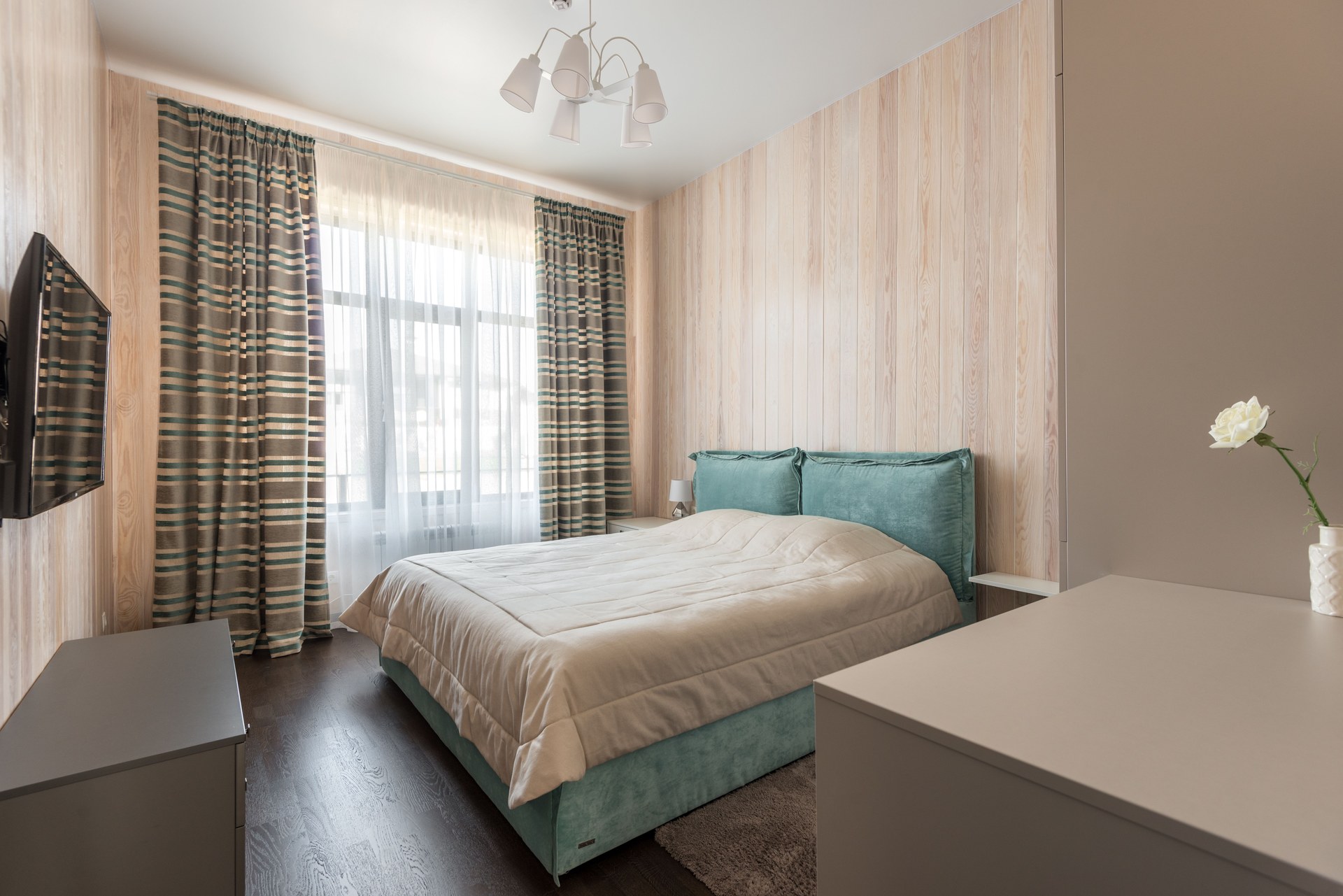 Minimalist bedroom with aqua bedding and striped curtains, featuring a cozy bed and natural light
