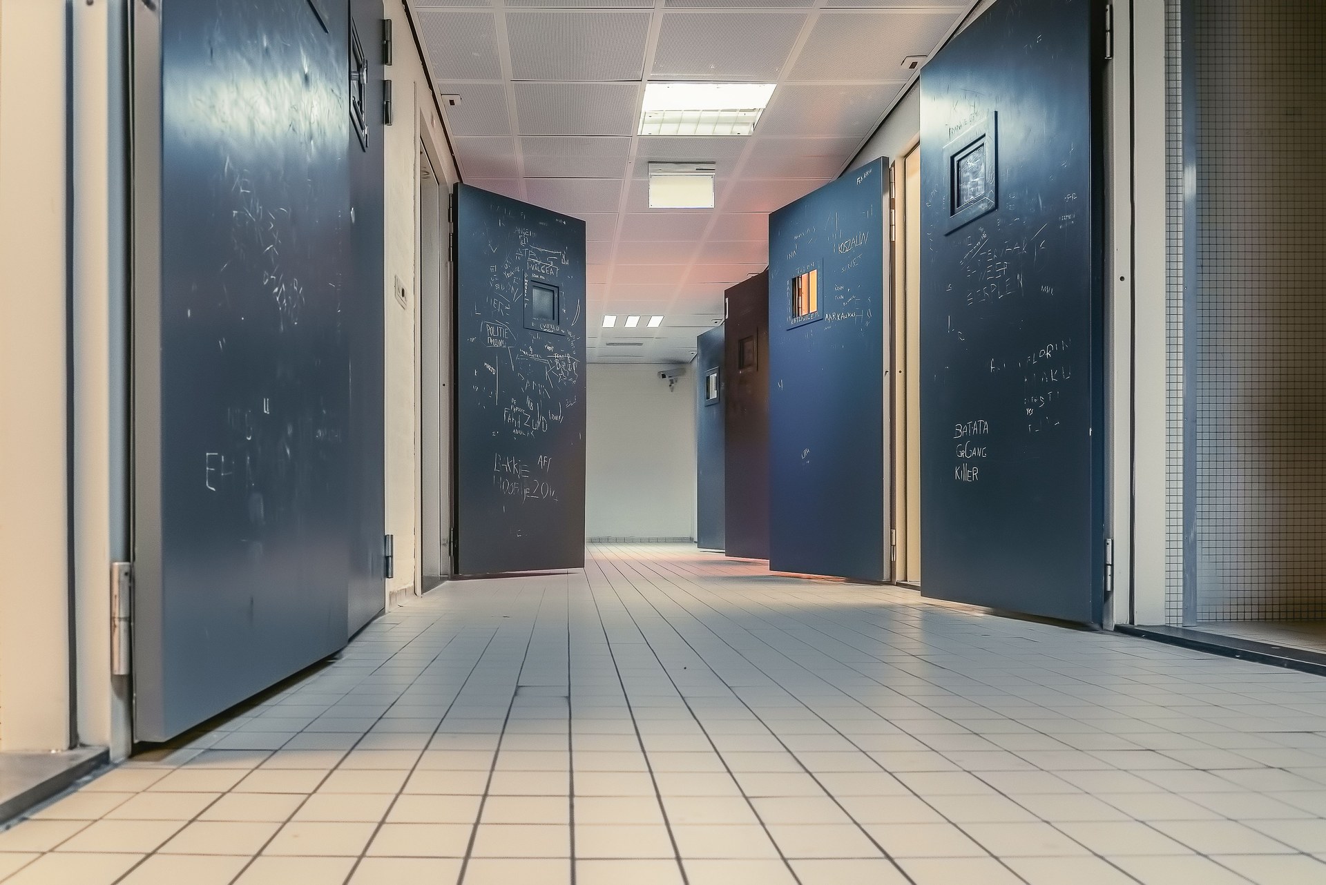 Low angle view of a modern hallway with open blue doors and white tiled flooring, creating a clean and tranquil environment