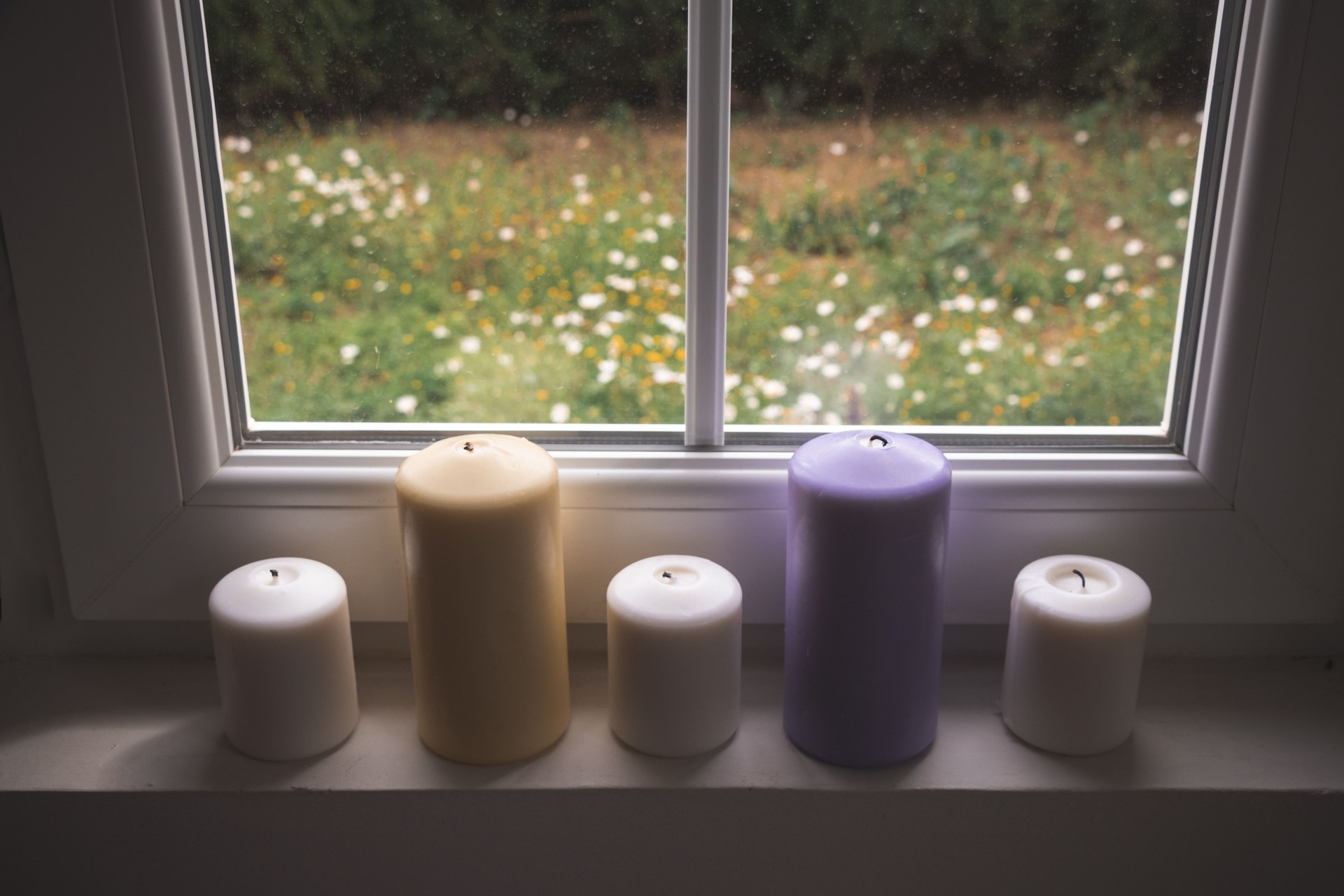 View of colorful candles on a windowsill overlooking a garden. Perfect for relaxation themes
