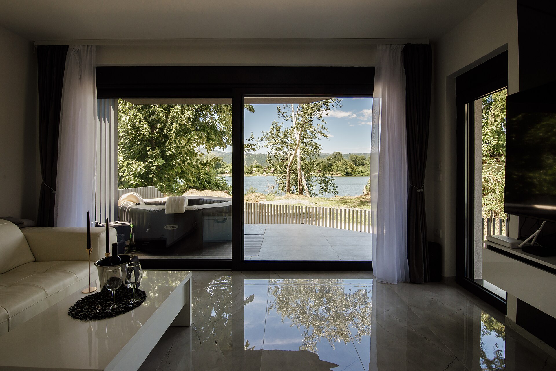 Modern living room with large windows showing view of trees and lake in daylight, illustrating What Does Feng Shui Say About Sharp Corners on Furniture