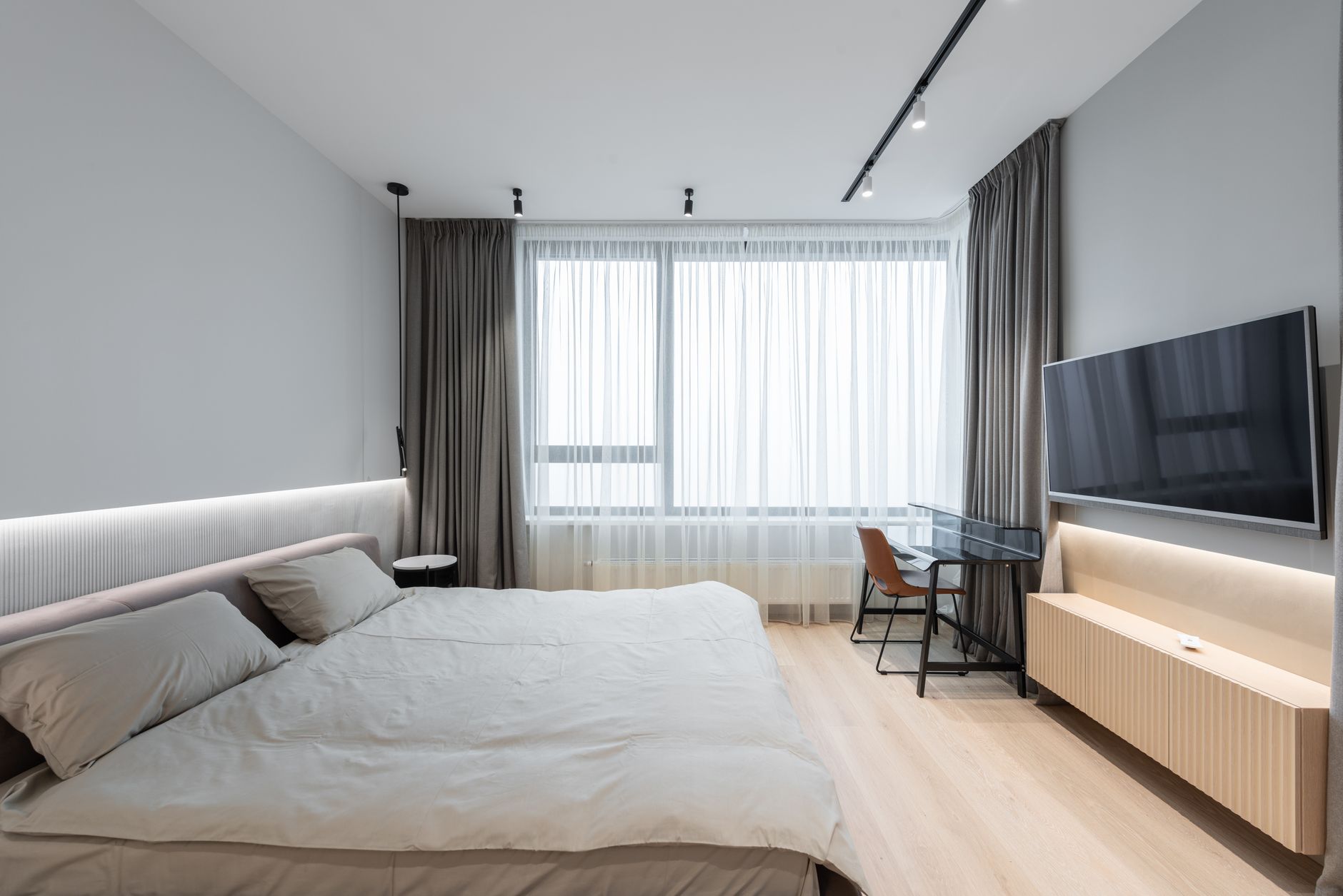 Interior of modern bedroom with bed next to TV on wall with curtains on window and table with chair, illustrating Sloped Ceiling Bedroom: A Feng Shui Guide to the Layout