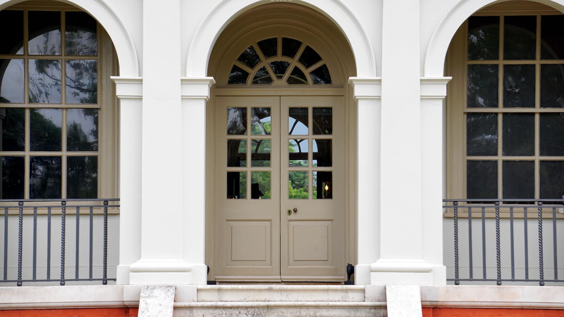 Front view of a classic white building entrance with arched doorway and columns, featuring glass windows and metal railings, illustrating Staircase Facing the Front Door: What Feng