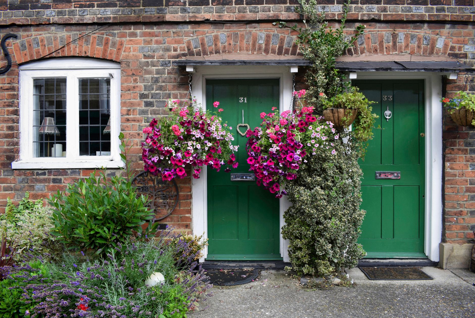 Front view of a residential brick house with green doors and vibrant flower arrangements, illustrating Staircase Facing the Front Door: What Feng Shui Says