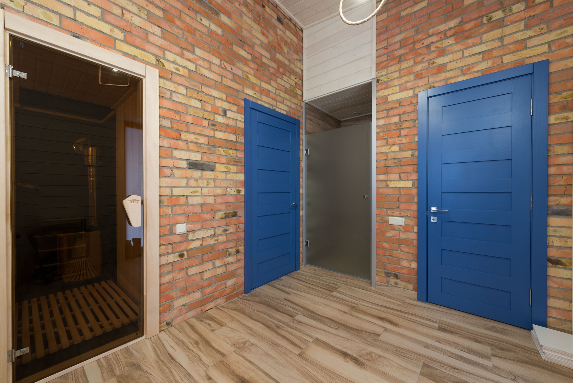 A stylish interior featuring blue doors, brick walls, and a sauna room in a cozy home setting, illustrating What Feng Shui Says About Doors That Stick or Squeak