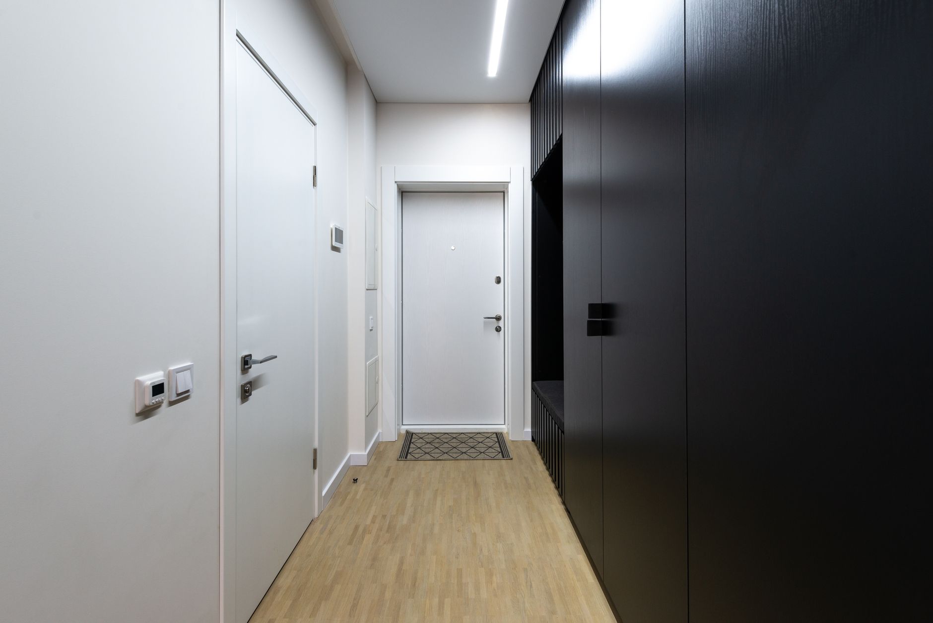 Interior of empty hallway with white doors and black wardrobe under luminous lamp on ceiling, illustrating What Feng Shui Says About Doors That Stick or Squeak
