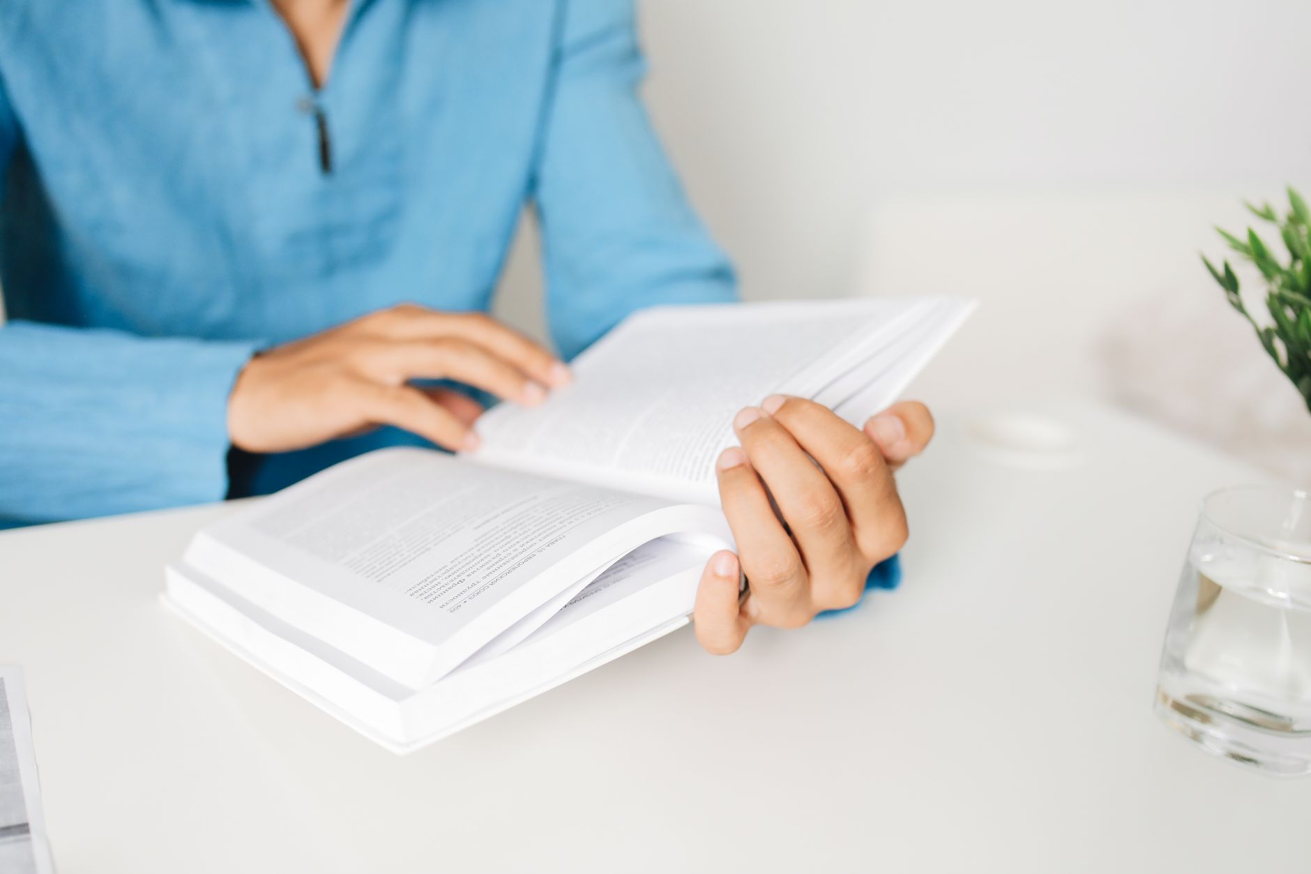 Person in a blue shirt studying a book at a white desk indoors with a plant, illustrating How Should a Study or Work Corner Be Arranged