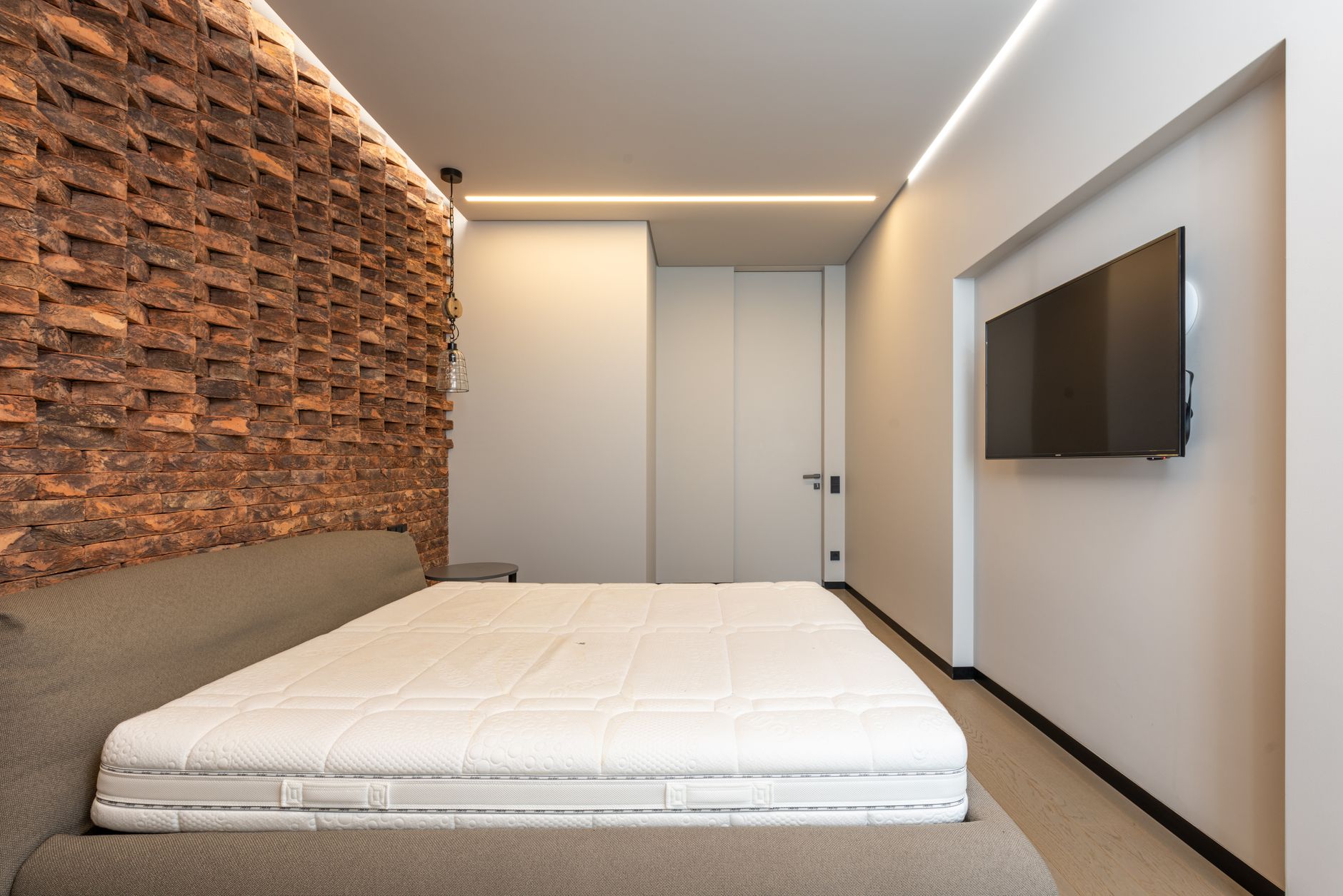 Comfortable be with soft mattress in stylish minimalist bedroom with modern TV and creative brick wall, illustrating What Does Feng Shui Say About Symmetry in a Bedroom