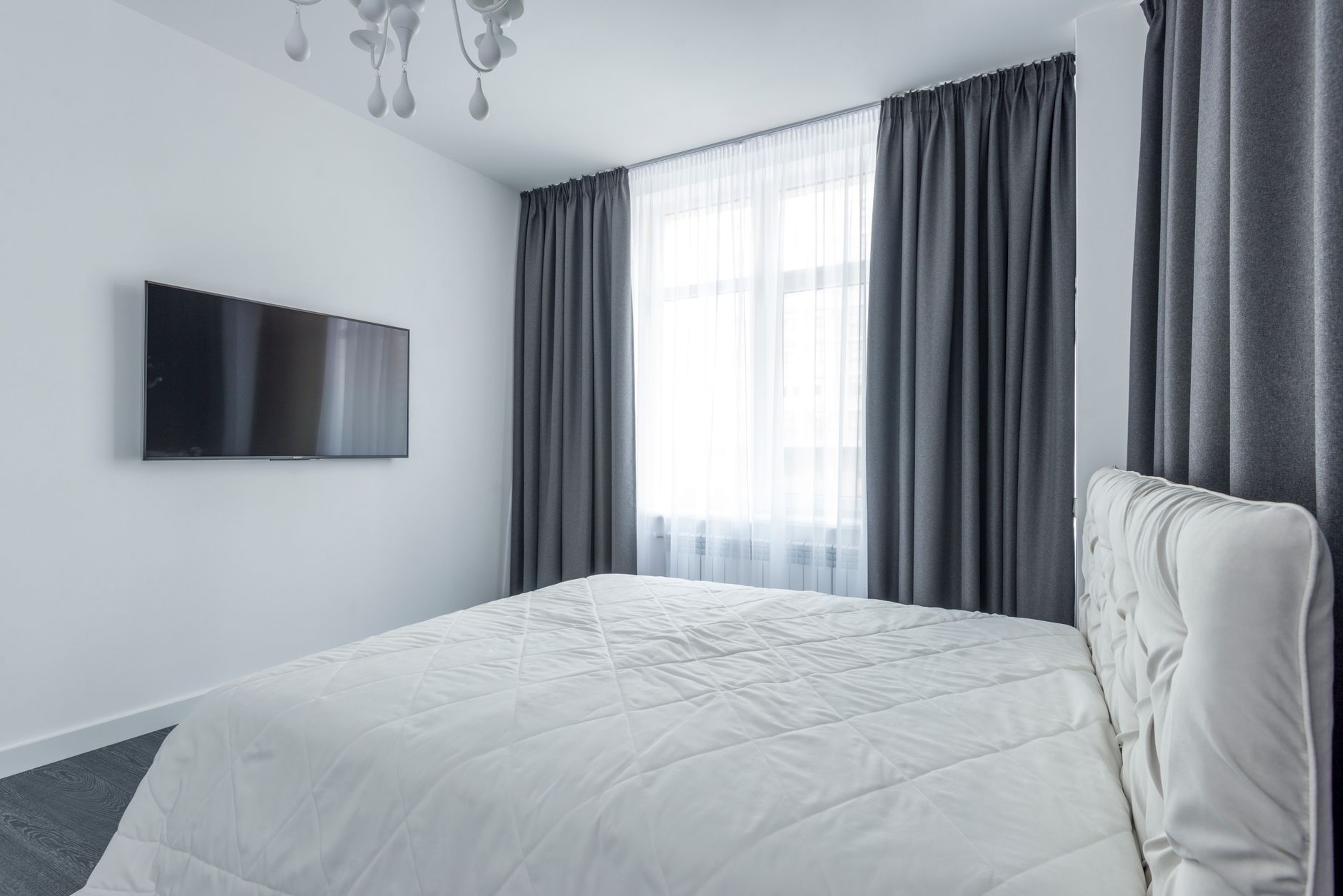 A modern bedroom featuring minimalist decor with a flat screen TV and elegant curtains, illustrating What Does Feng Shui Say About Symmetry in a Bedroom