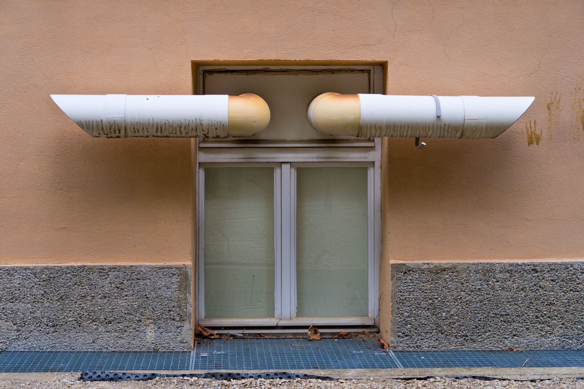 Close up of industrial ventilation pipes above a window on a building wall, illustrating What Does Feng Shui Say About Ventilation and Stale Air