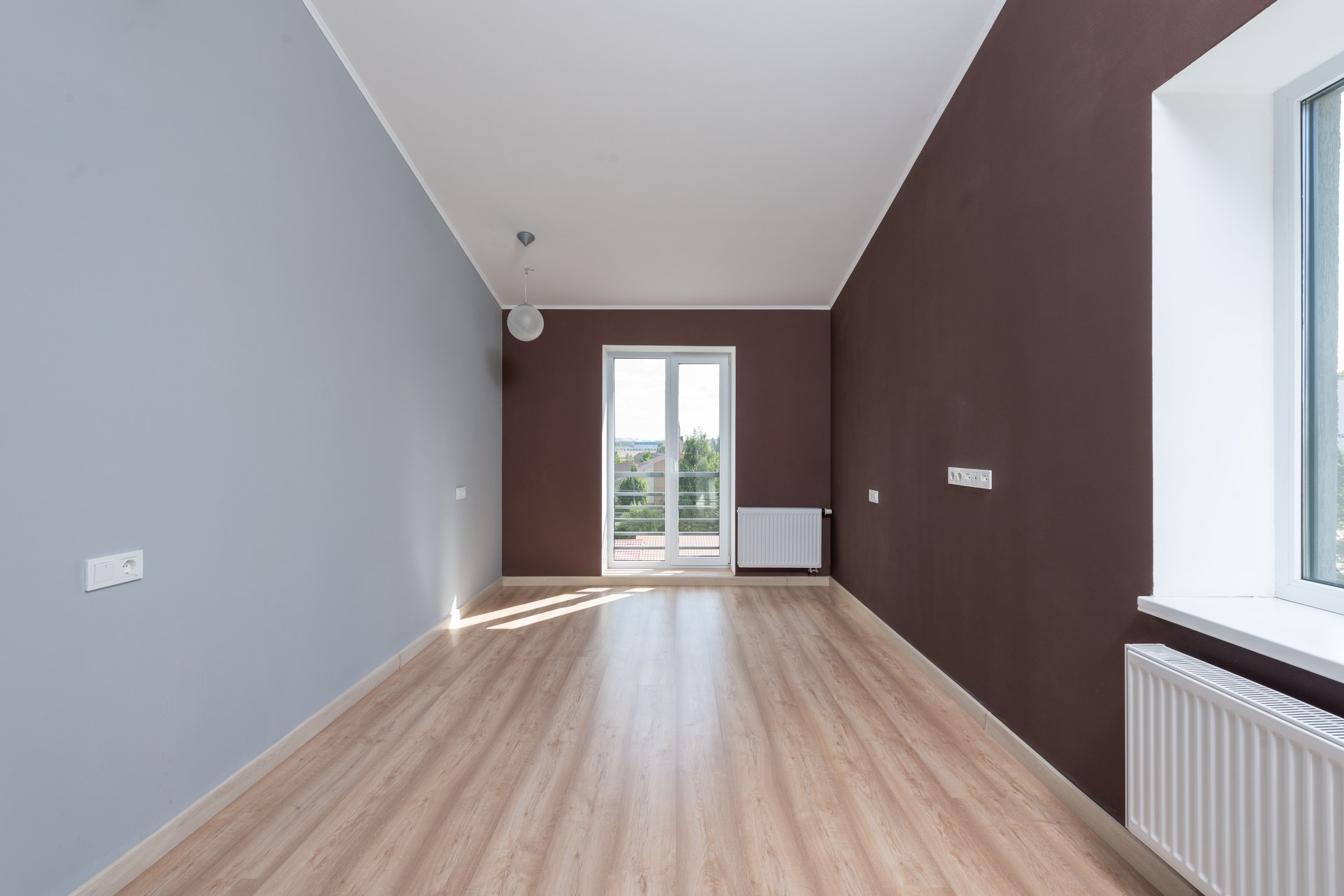 Spacious empty room featuring wooden flooring and a large window with natural light