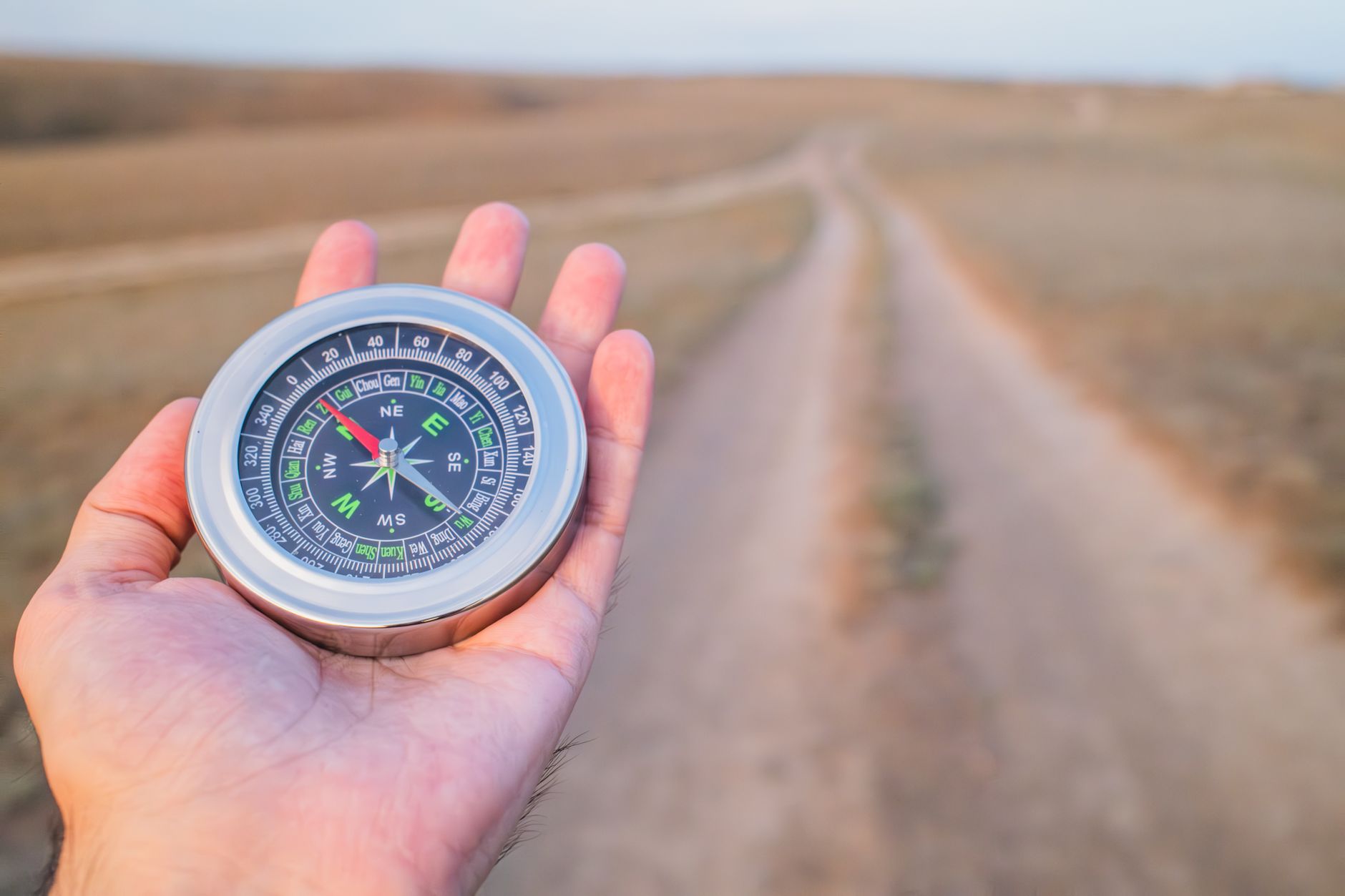 Hand holding a compass guiding along a dusty path outdoors. Perfect for travel and exploration themes, illustrating What Is a Feng Shui Compass, and Do You Need One