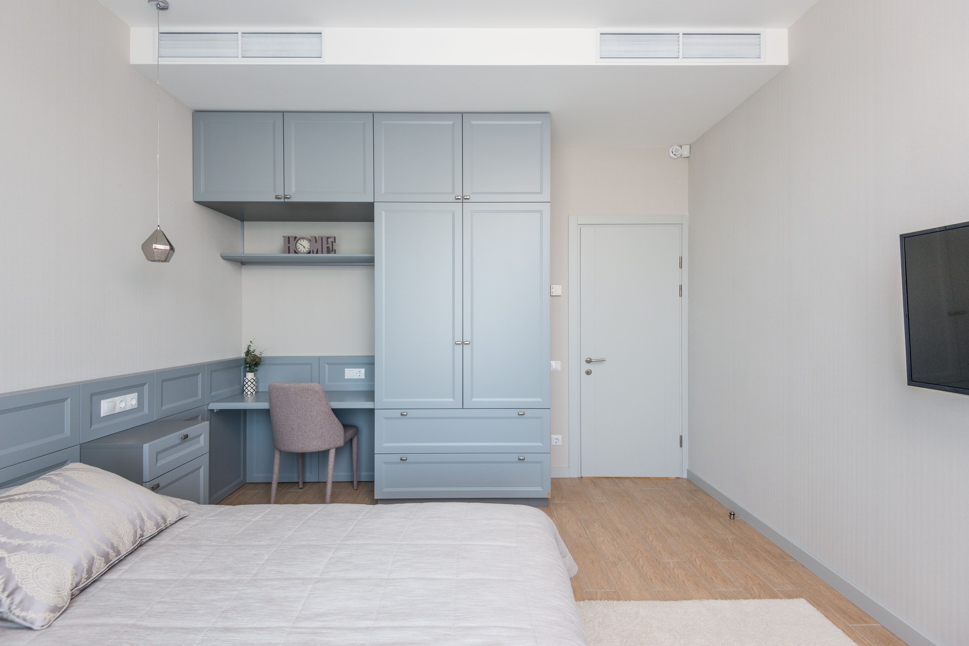 A sleek and modern bedroom with an integrated workspace featuring pastel blue cabinetry