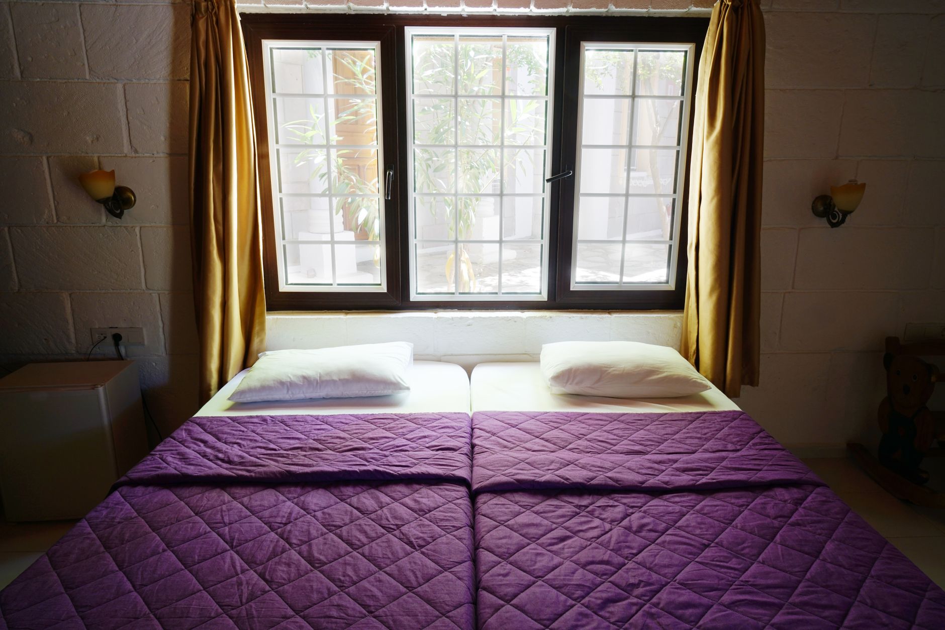 Inviting bedroom featuring purple bedding, natural light through a window, and warm decor, illustrating What Should Be Under the Bed in Feng Shui, and What Shouldn't