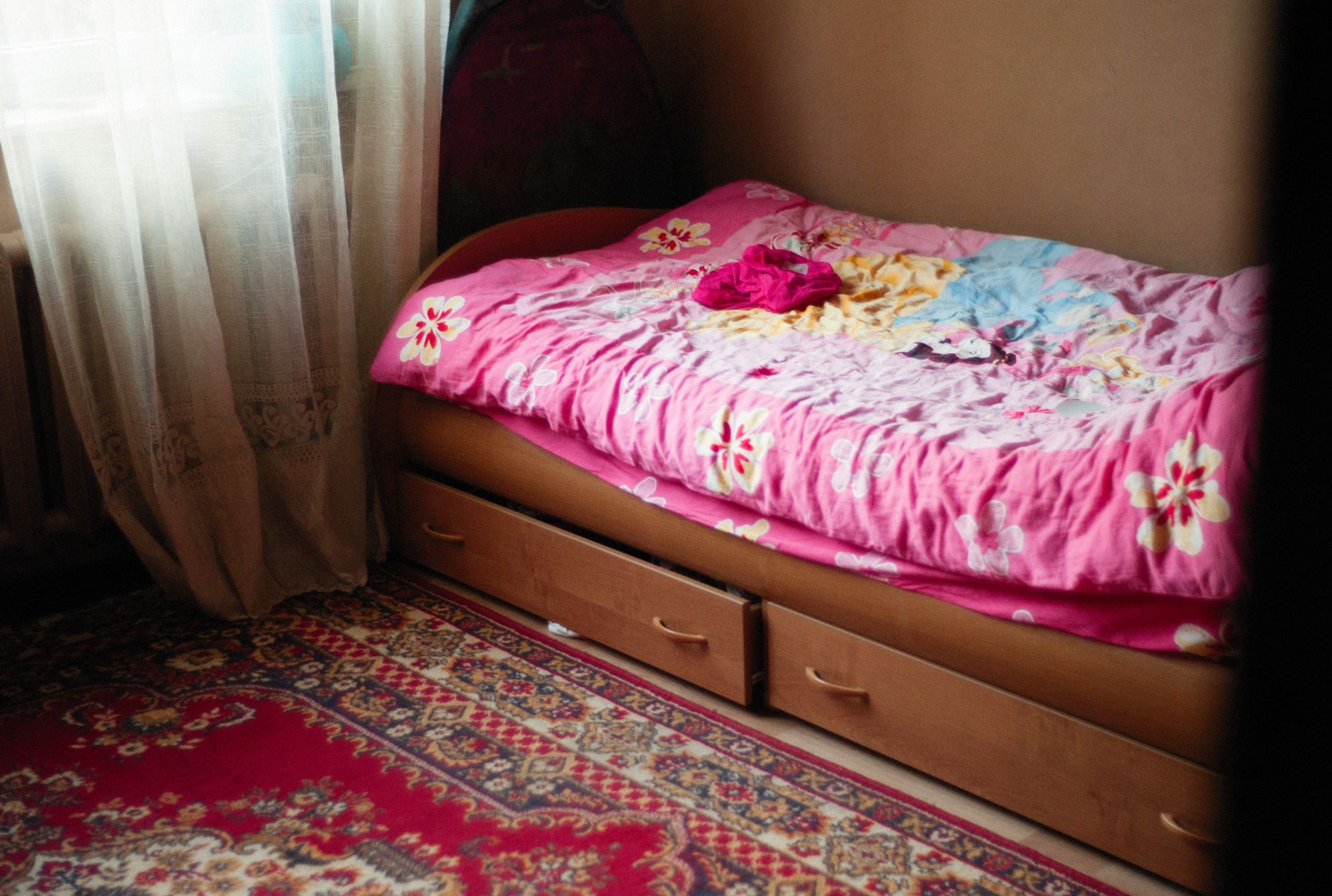 A warm and inviting bedroom scene featuring a floral pink bedspread, under bed drawers, and a patterned rug, illustrating What Should Be Under the Bed in Feng Shui, and What Should