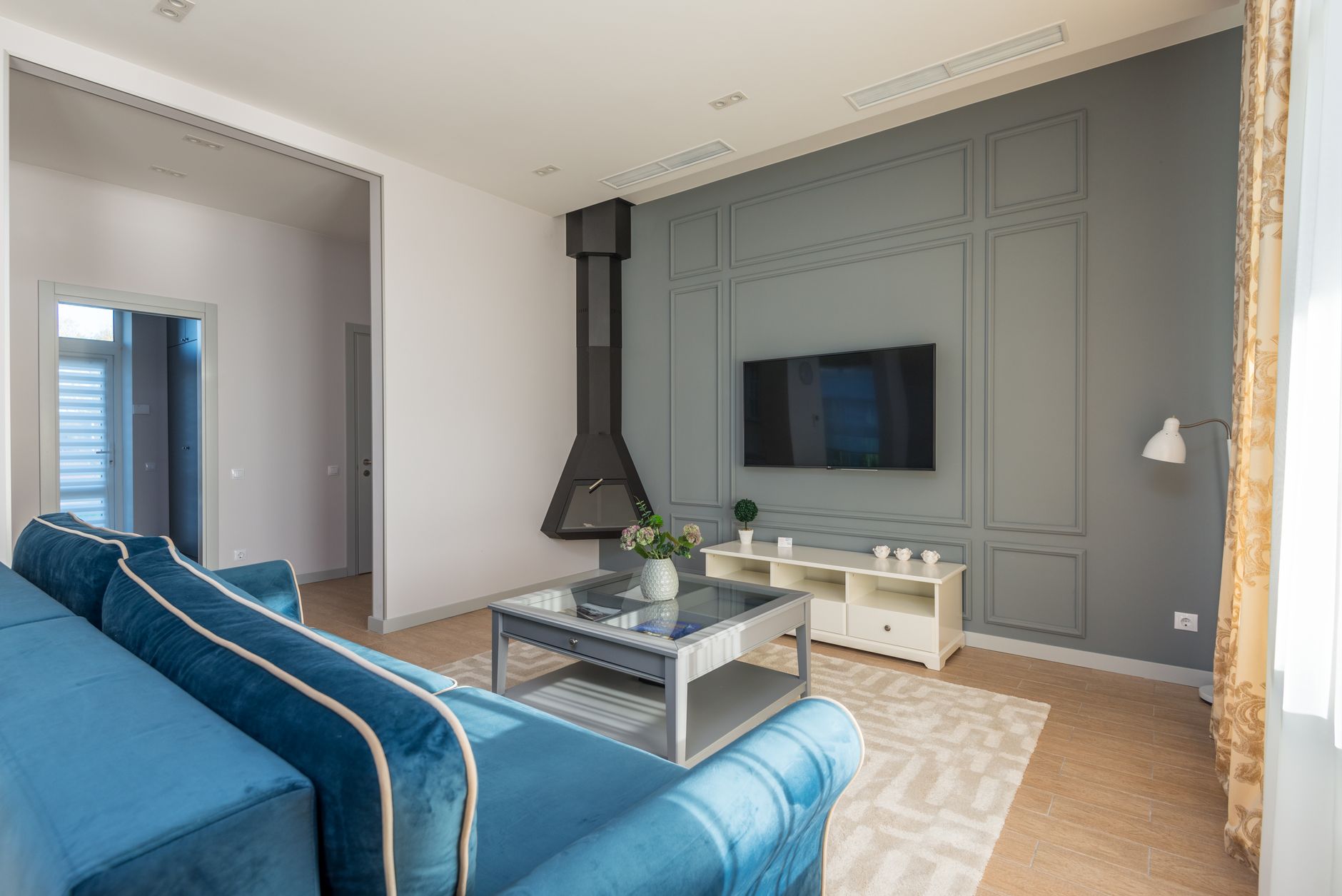 A stylish living room featuring a blue couch, wall mounted TV, and elegant decor, illustrating Where Should a Sofa Go in a Living Room? Feng Shui Guide