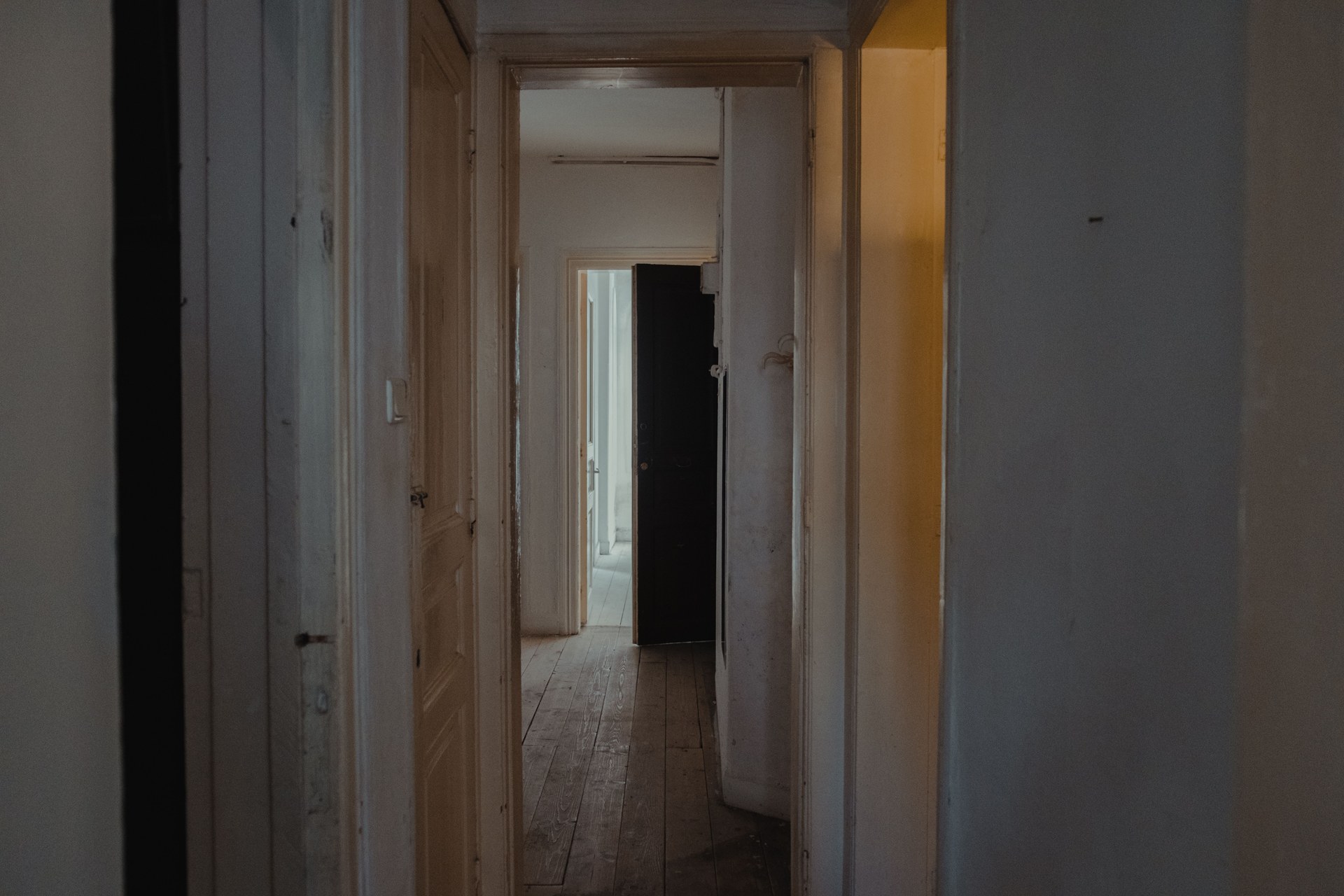 A dimly lit hallway in an apartment with wooden doors and a rustic feel