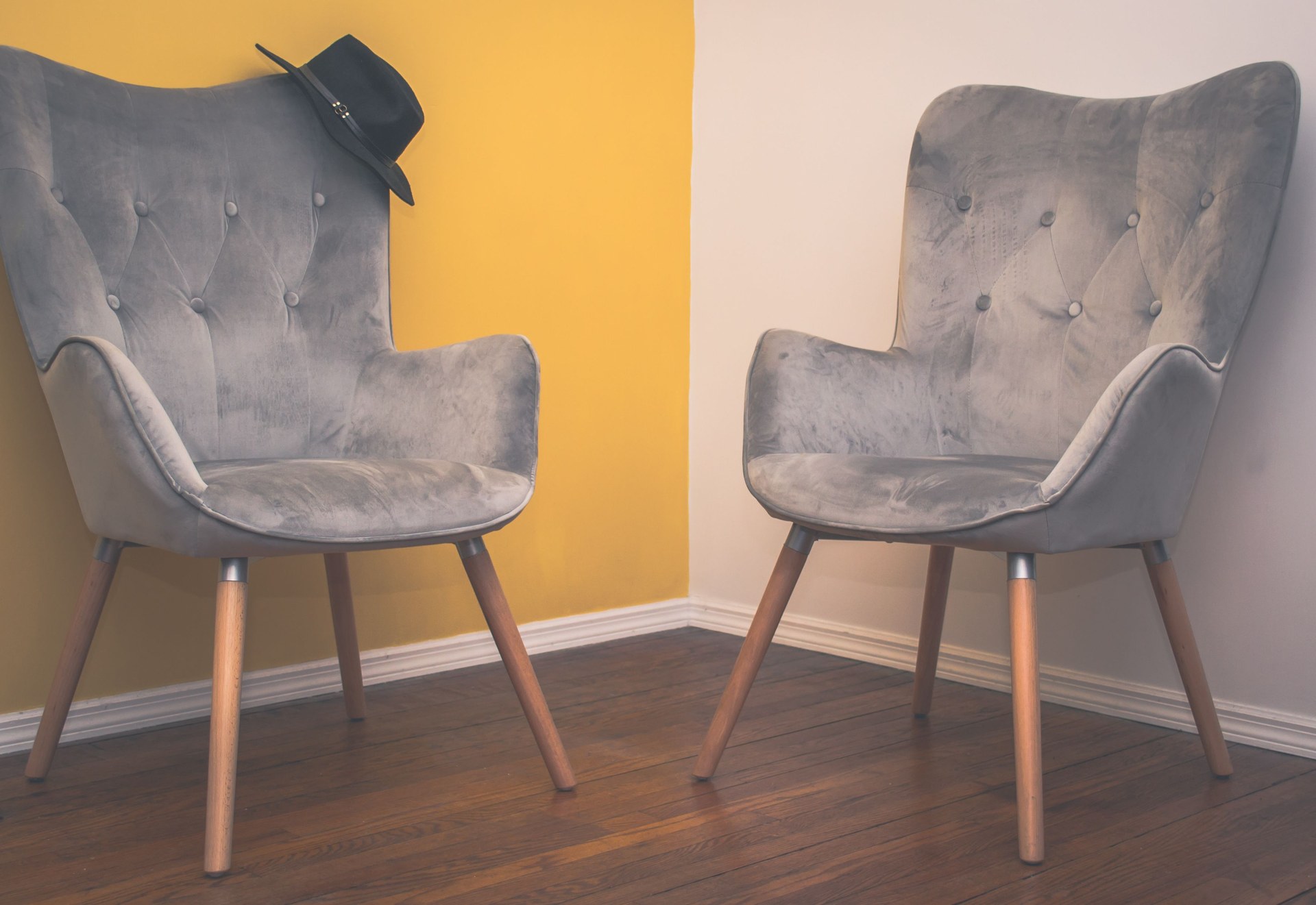 Two contemporary gray armchairs in a minimalist interior with a yellow accent wall and wooden flooring
