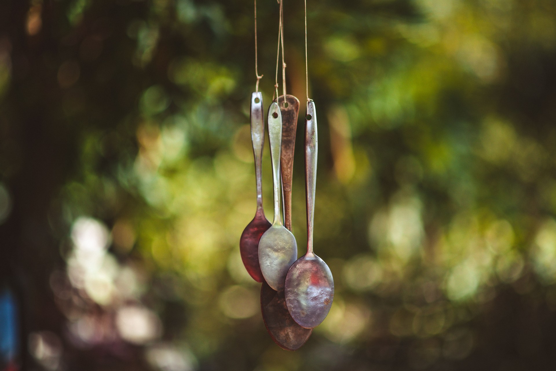 Handmade wind chime made from reused spoons, hanging outdoors with a blurred nature background
